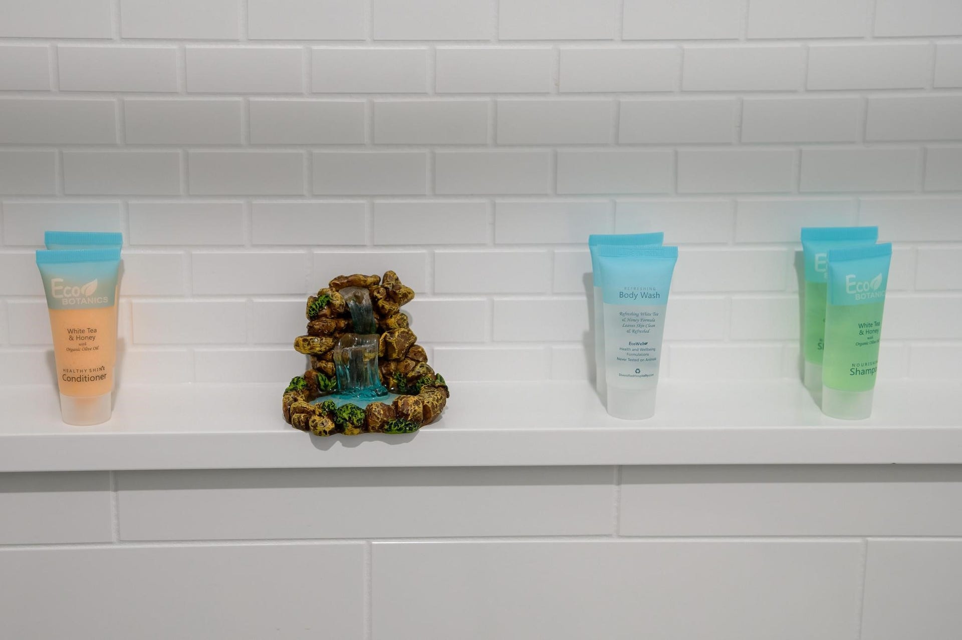 1301 Bright Hill Drive, Katy, TX 77493 A stylish bathroom shelf features neatly arranged toiletries and a charming miniature waterfall accent against a sleek white subway tile backdrop.