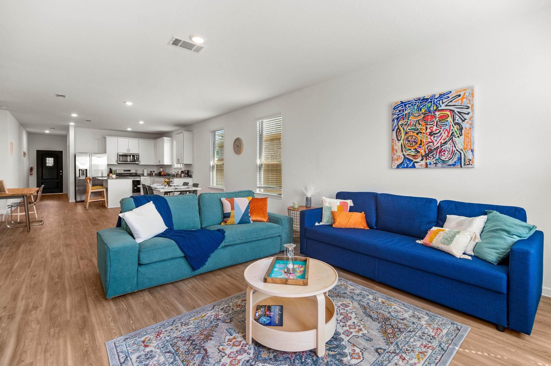 1301 Bright Hill Drive, Katy, TX 77493 Bright and inviting open-concept living area features stylish blue sofas, vibrant artwork, and a cozy rug, seamlessly flowing into a modern kitchen with sleek white cabinetry and stainless steel appliances.