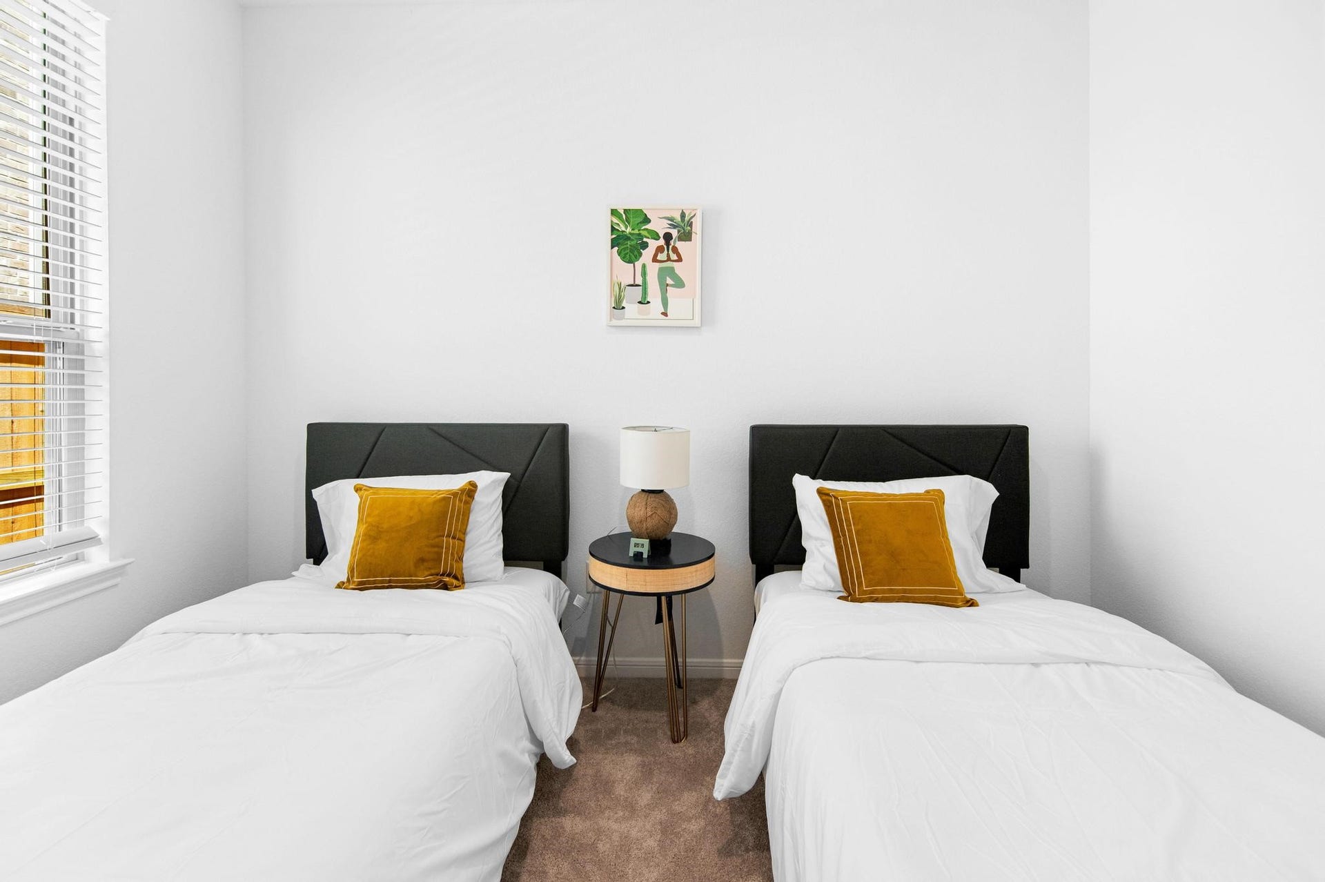 1301 Bright Hill Drive, Katy, TX 77493 Charming bedroom with two twin beds, each adorned with a mustard accent pillow, flanked by a stylish round nightstand and lamp, all bathed in natural light from a large window.