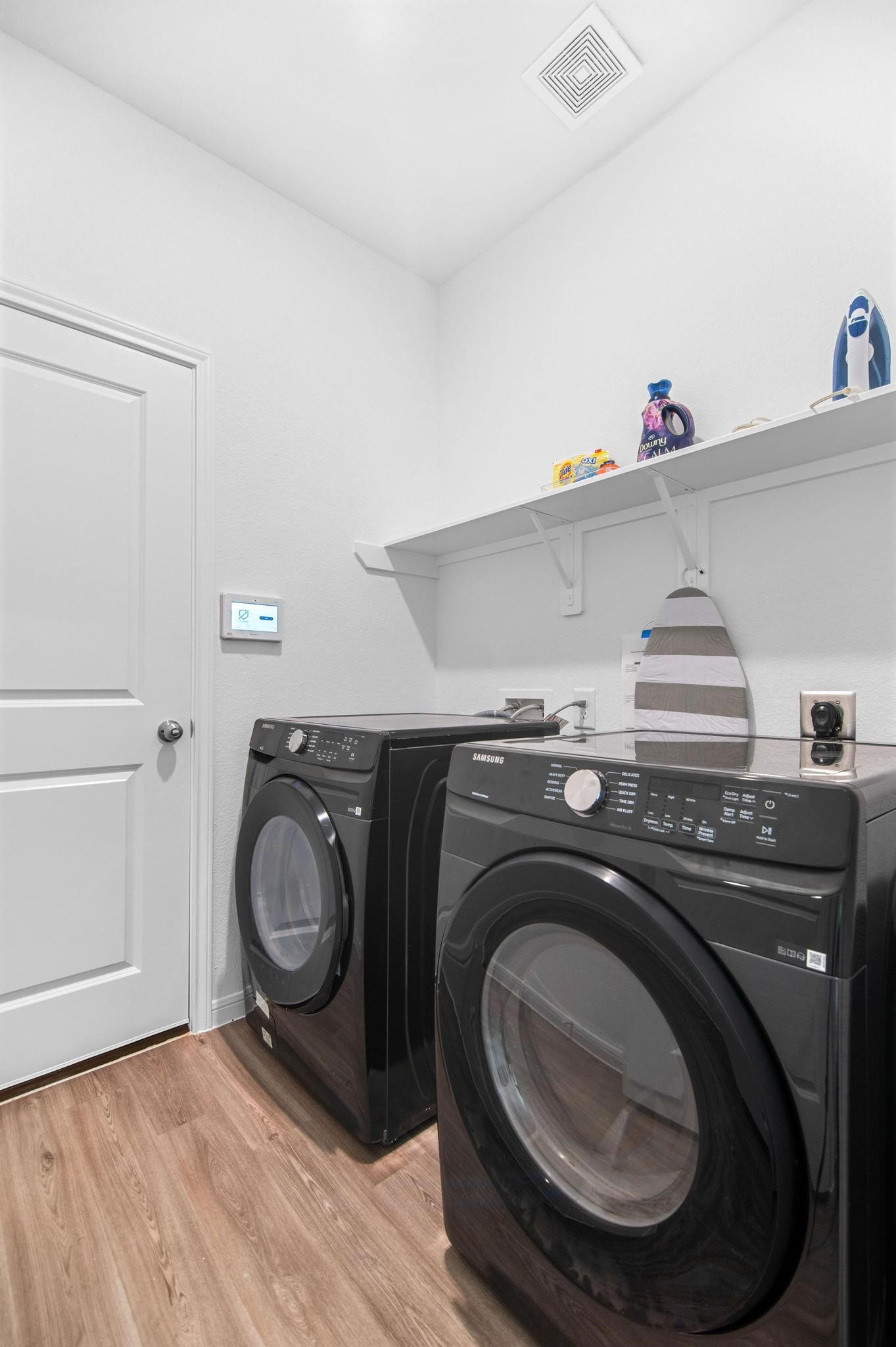 1301 Bright Hill Drive, Katy, TX 77493 Modern laundry room featuring sleek black Samsung washer and dryer, ample shelving, and stylish wood flooring.