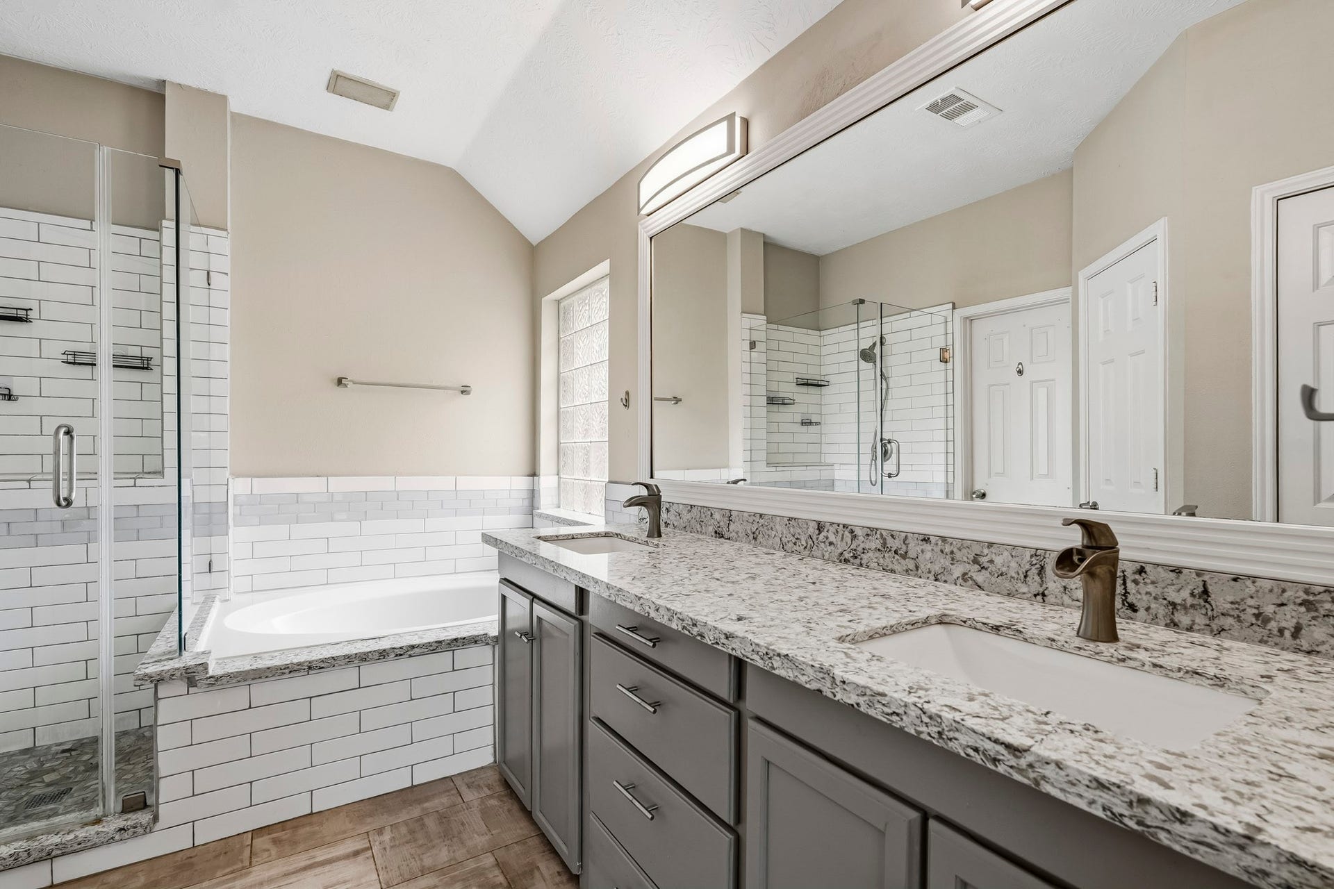 Updated primary bath featuring dual sinks, a relaxing soaking tub, and a separate frameless glass shower.