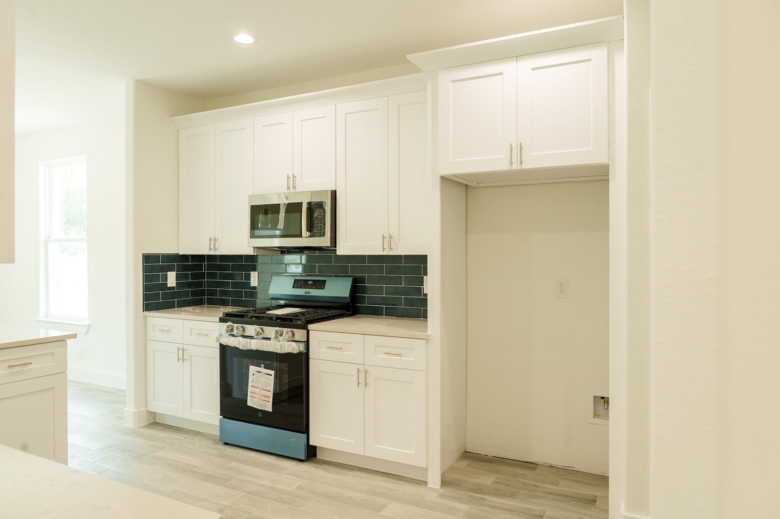2306 Ridgewood Drive Drive, West Columbia, TX 77486 Modern kitchen featuring sleek white cabinetry, a stainless steel microwave, and a stylish dark tile backsplash.