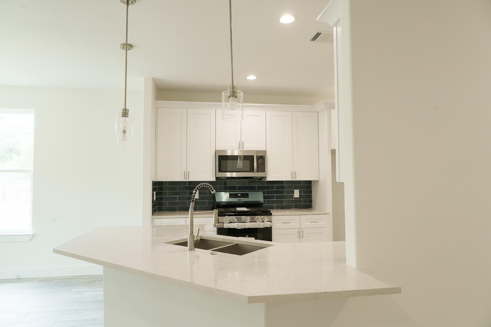 2306 Ridgewood Drive Drive, West Columbia, TX 77486 Modern kitchen featuring sleek white cabinetry, a stylish black tile backsplash, and contemporary pendant lighting above a spacious quartz island with a dual sink.