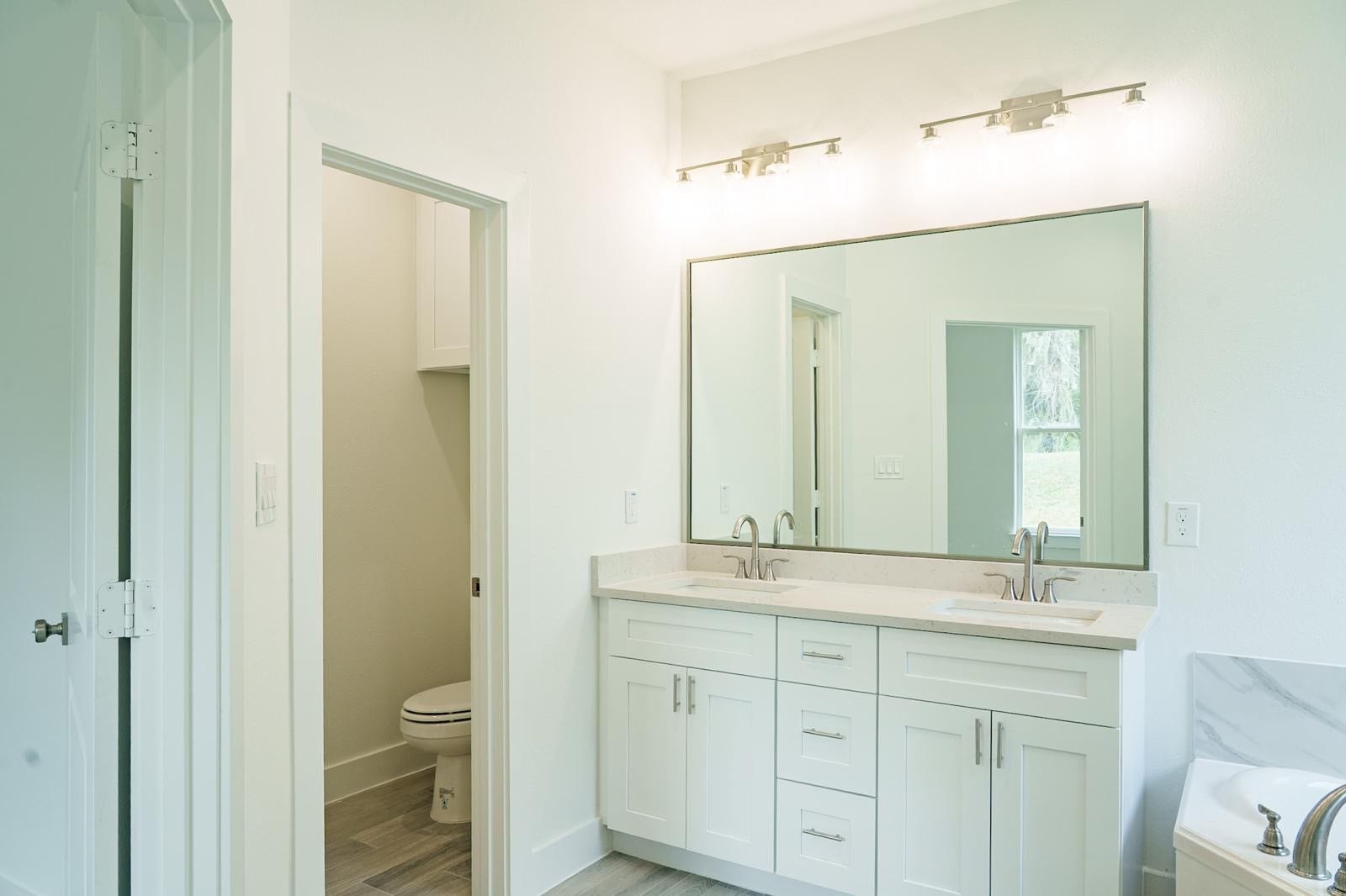 2306 Ridgewood Drive Drive, West Columbia, TX 77486 Bright and modern bathroom featuring a double vanity with sleek fixtures, a large mirror, and ample storage, complemented by a separate toilet area for added privacy.