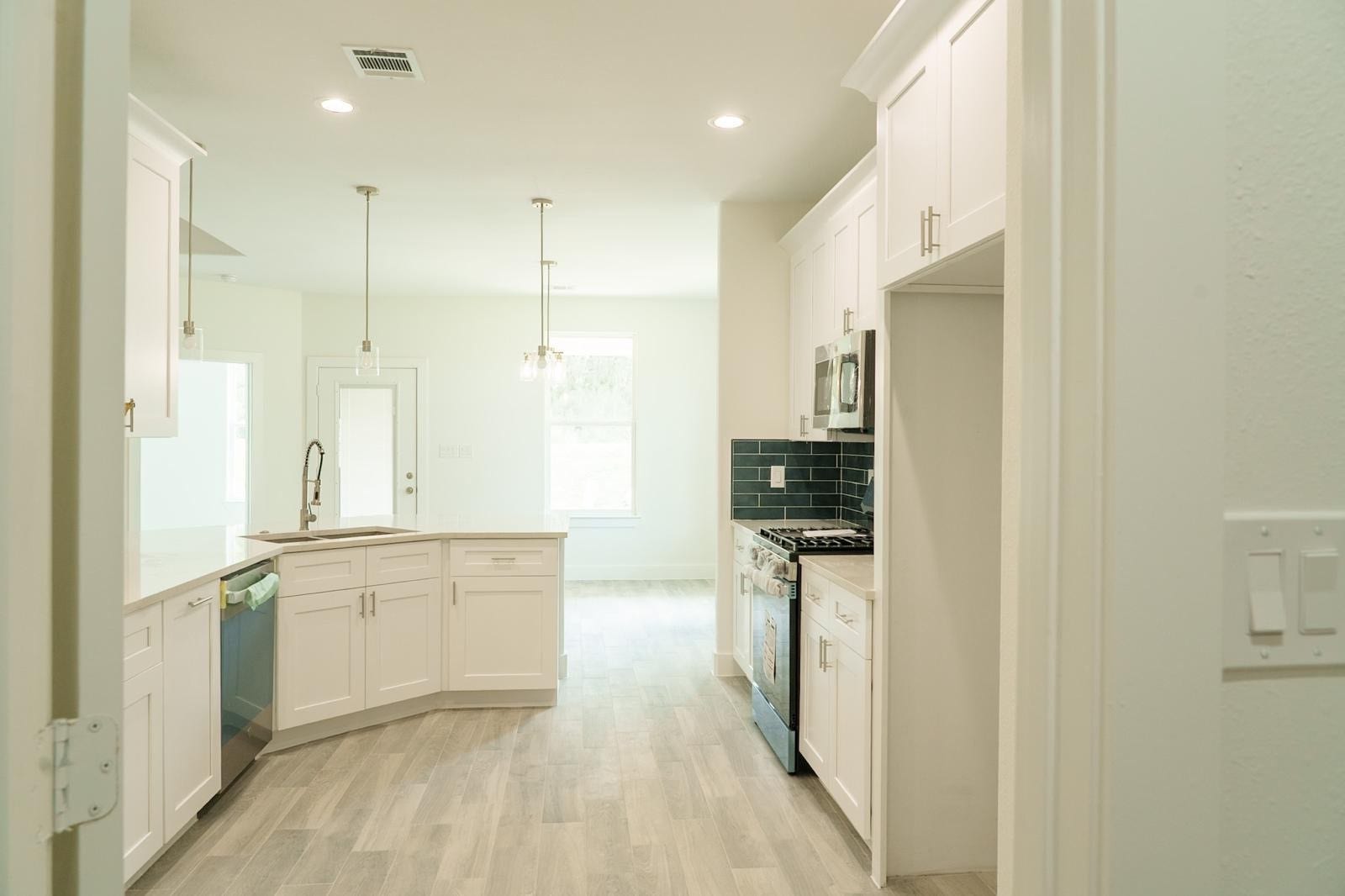 2306 Ridgewood Drive Drive, West Columbia, TX 77486 Bright and modern kitchen featuring sleek white cabinetry, stainless steel appliances, and elegant pendant lighting, complemented by a stylish dark backsplash and light wood flooring.