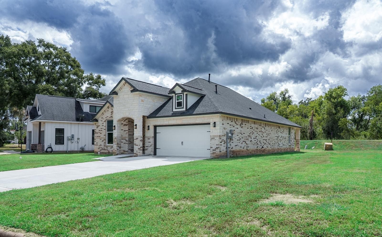 2306 Ridgewood Drive Drive, West Columbia, TX 77486 A brick home with a gabled roof, spacious two-car garage, and lush green lawn, set against a backdrop of mature trees and an expansive sky.