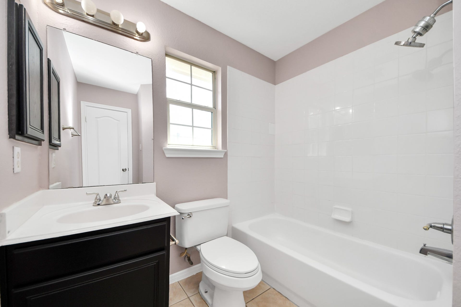 10026 Gil Jr Lane, Houston, TX 77075 Bright and inviting bathroom featuring a sleek vanity with ample storage, a classic bathtub with a shower, and a large window providing natural light.