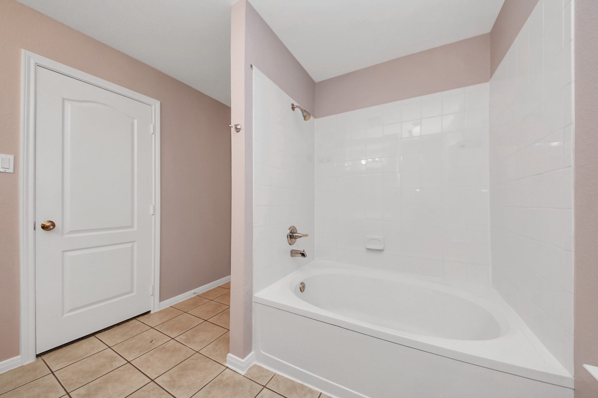 10026 Gil Jr Lane, Houston, TX 77075 Spacious primary bathroom featuring a sleek white bathtub with tiled surround and a neutral color palette, offering a clean and modern feel.