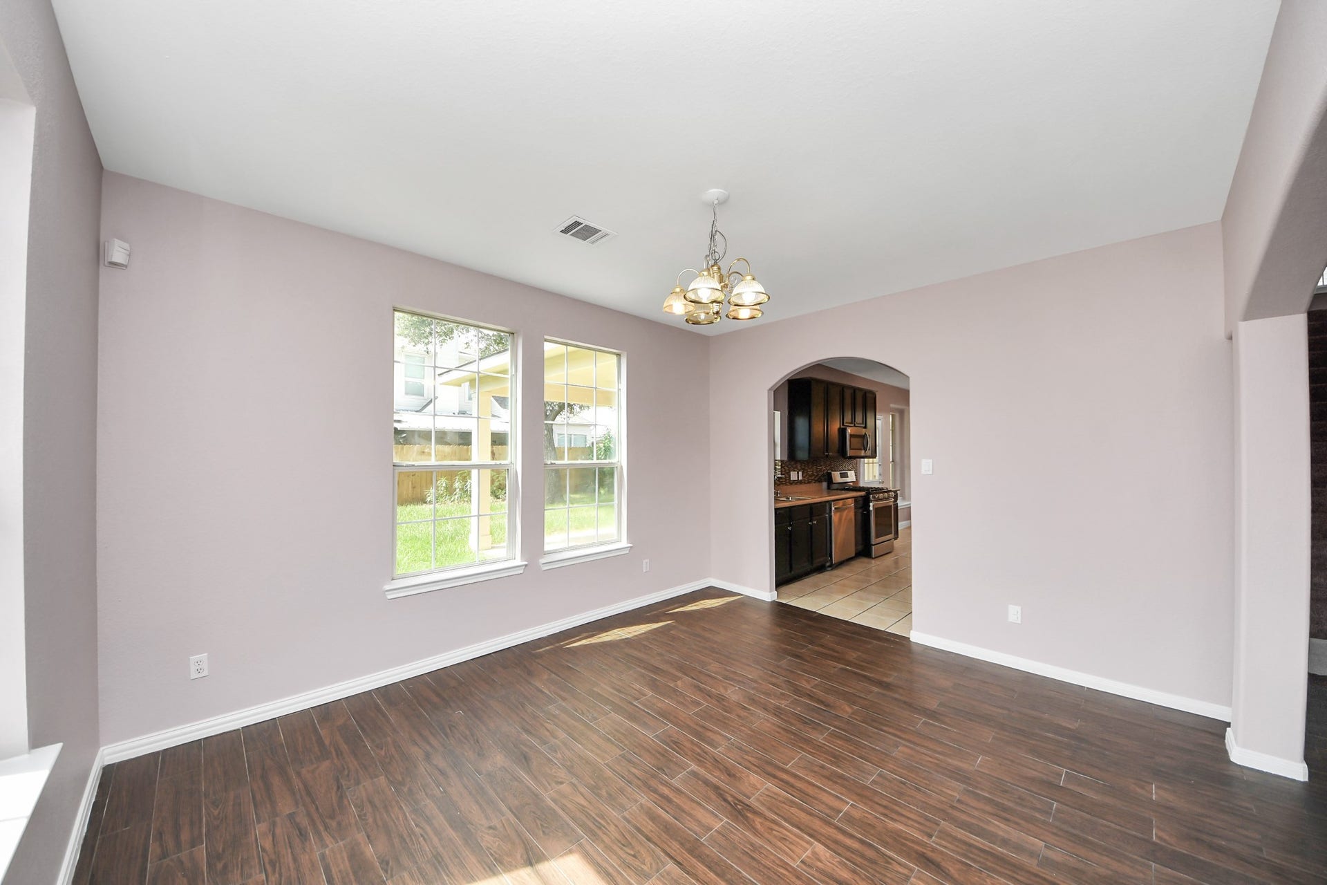 10026 Gil Jr Lane, Houston, TX 77075 Bright and inviting dining area with elegant wood-style flooring and large windows, seamlessly connected to a modern kitchen through an arched doorway.