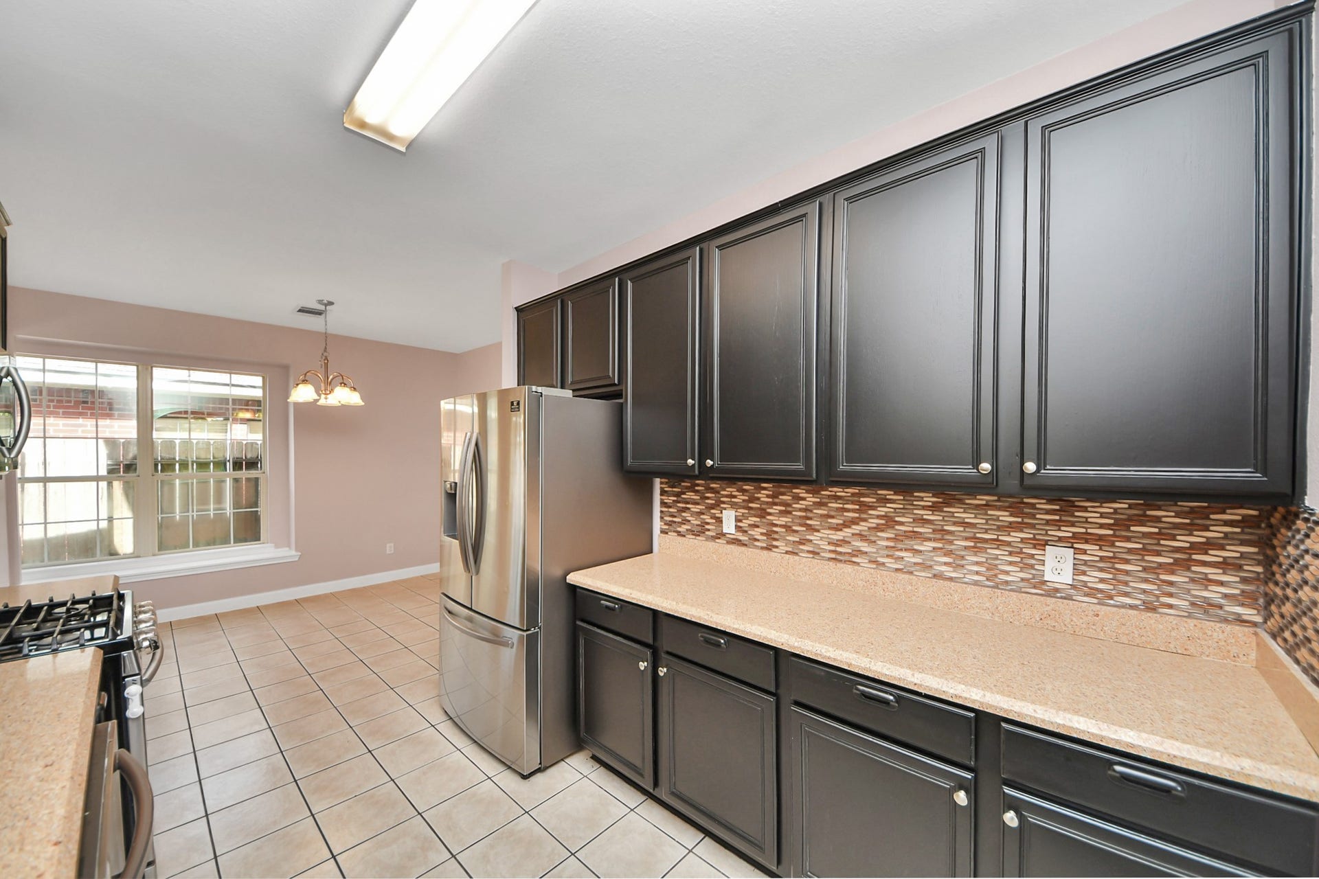 10026 Gil Jr Lane, Houston, TX 77075 Spacious kitchen with sleek dark cabinetry, modern stainless steel appliances, and a stylish tile backsplash, leading to a bright dining area with large windows.