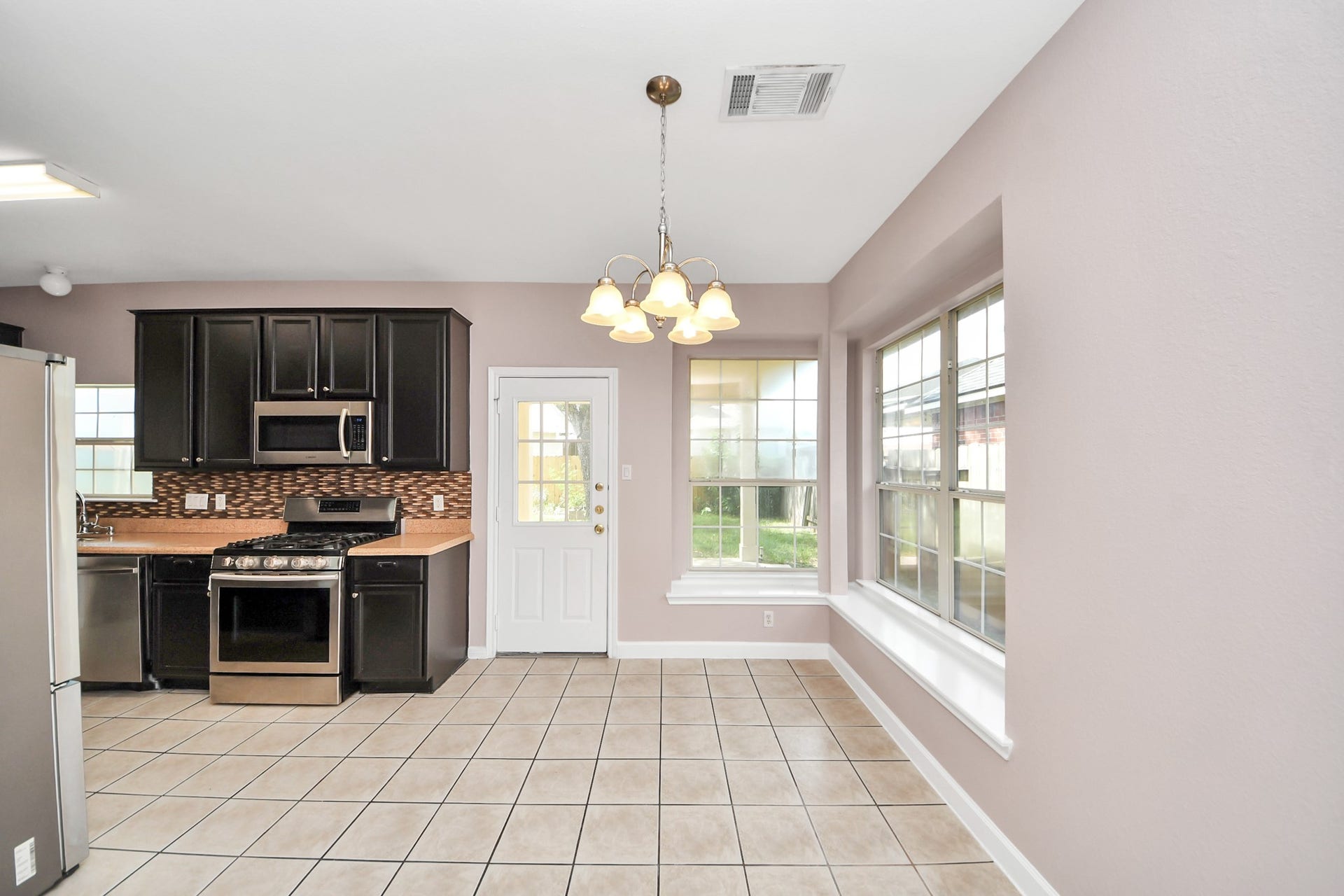 10026 Gil Jr Lane, Houston, TX 77075 Bright kitchen and dining area with modern dark cabinetry, stainless steel appliances, and large windows offering abundant natural light.