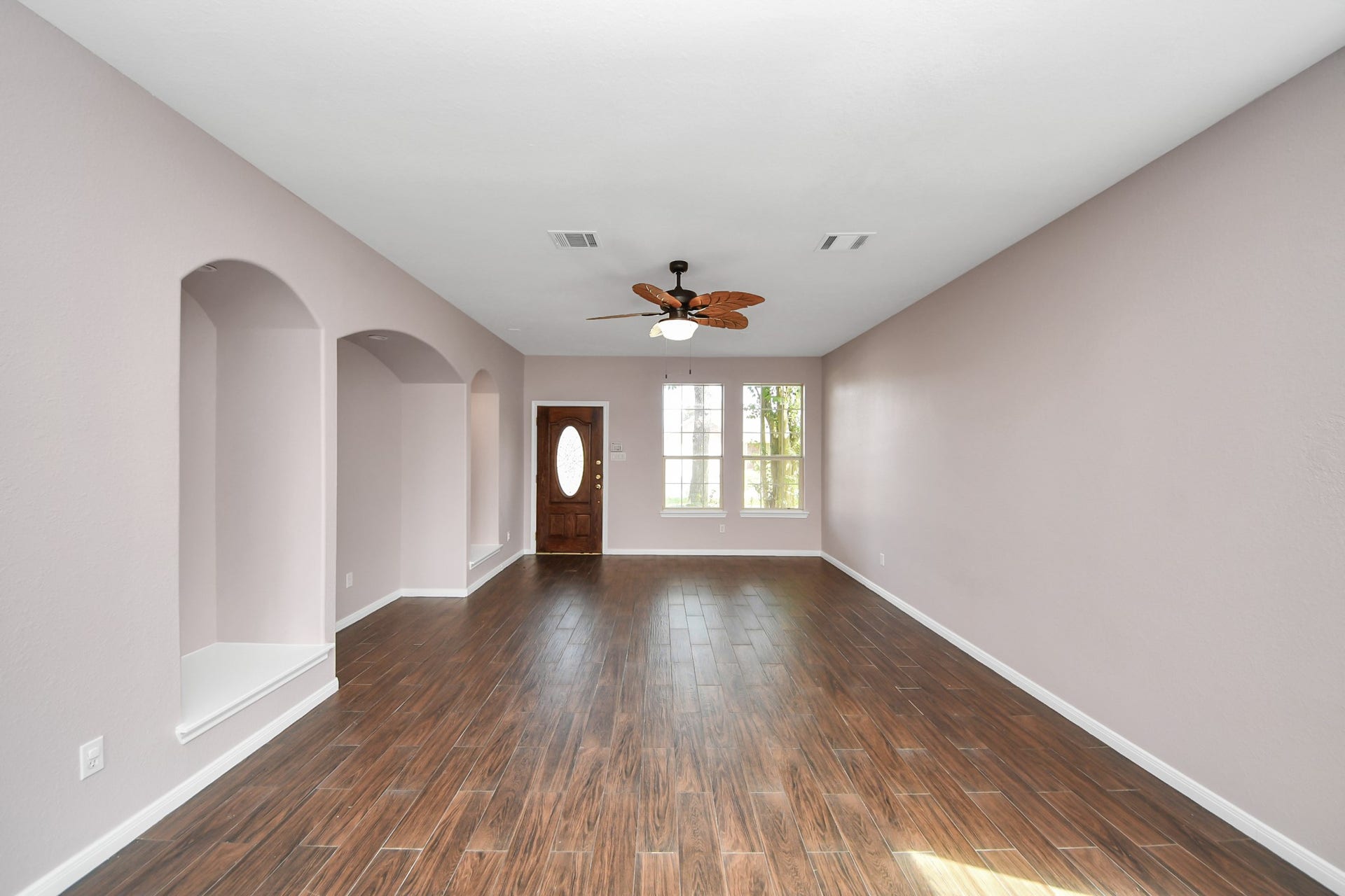 10026 Gil Jr Lane, Houston, TX 77075 Spacious living room with elegant wood flooring, soft neutral walls, and a stylish ceiling fan, featuring built-in wall niches and ample natural light from large windows.
