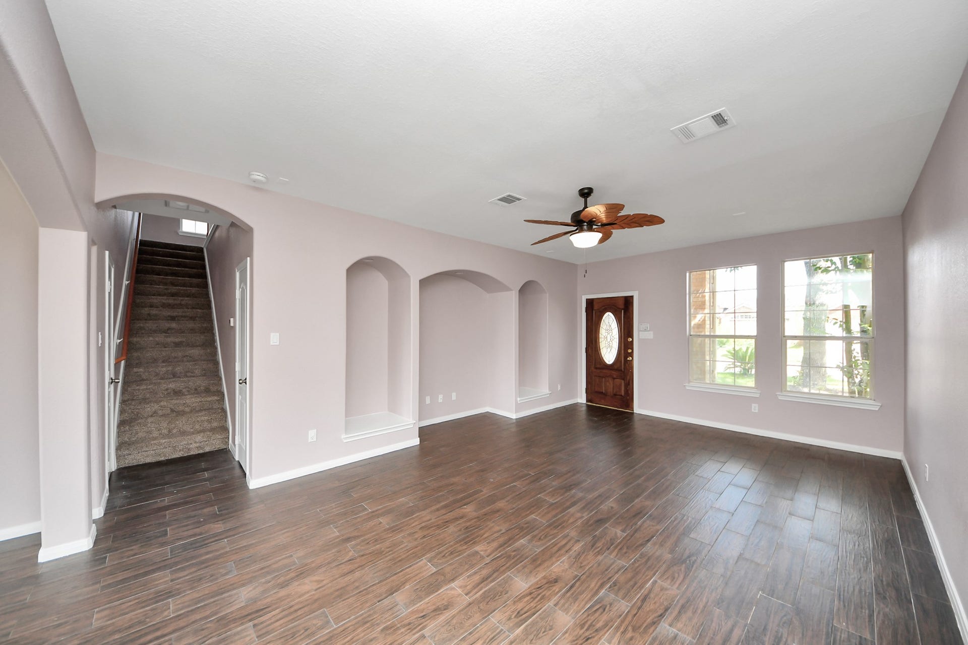 10026 Gil Jr Lane, Houston, TX 77075 Spacious living room featuring elegant wood-look flooring, recessed niches, and abundant natural light from large windows, complemented by a stylish ceiling fan and an inviting entryway.