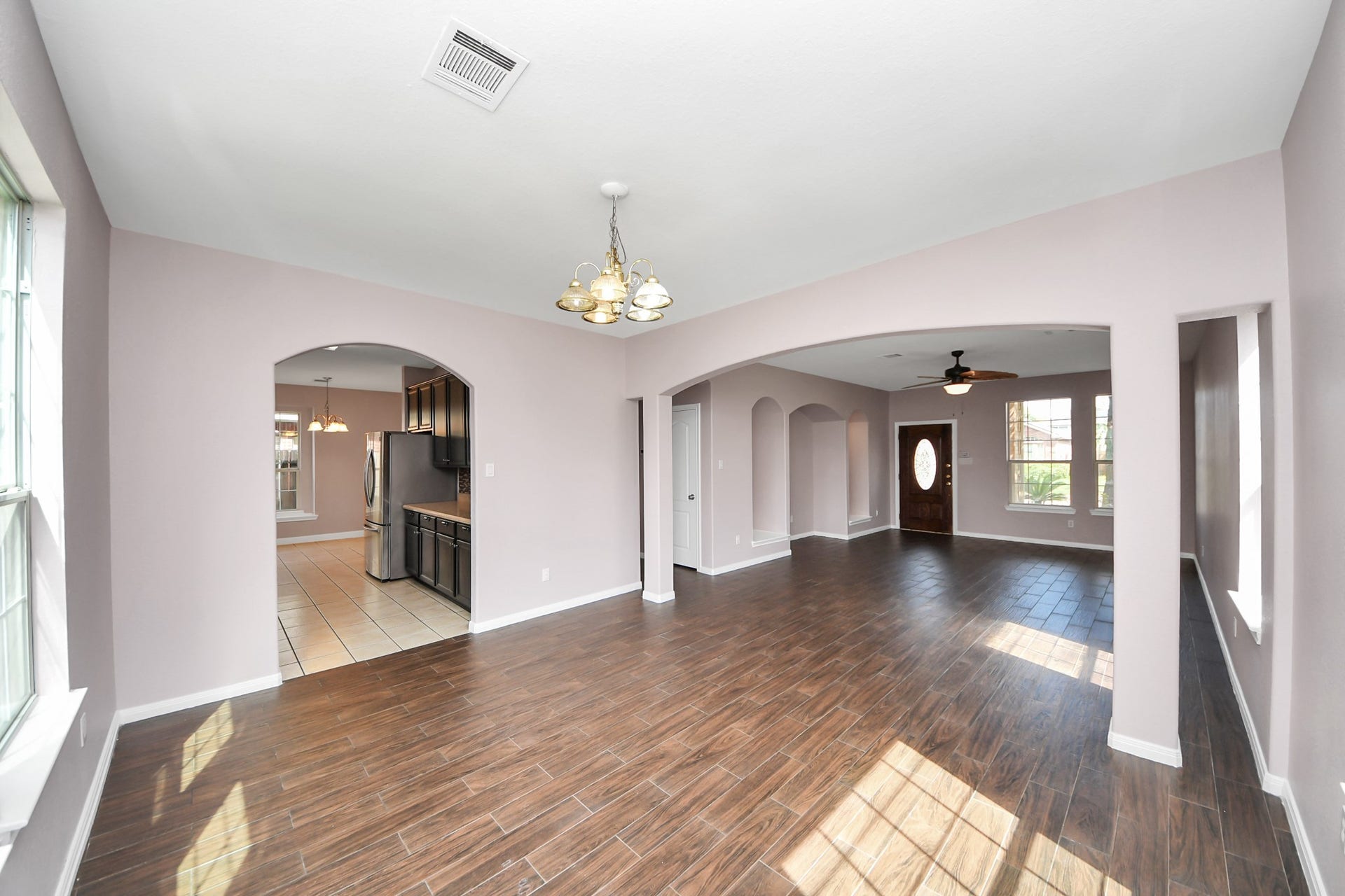 10026 Gil Jr Lane, Houston, TX 77075 Spacious open-concept living area with elegant wood-look flooring, archways leading to a modern kitchen, and ample natural light from large windows.