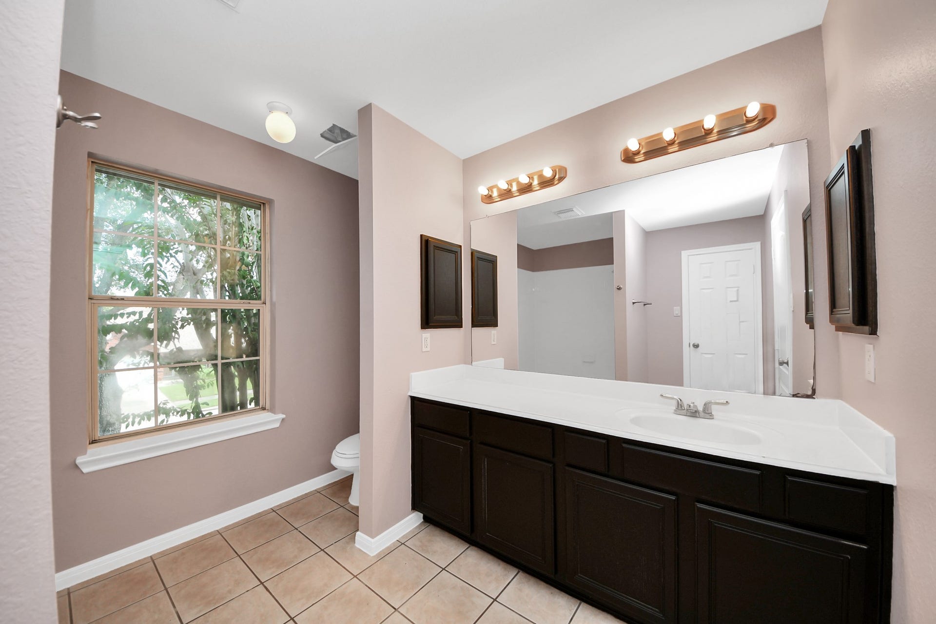 10026 Gil Jr Lane, Houston, TX 77075 Spacious primary bathroom featuring a large vanity with dual sinks, elegant lighting, and a window that brings in natural light, complemented by a soothing color palette.