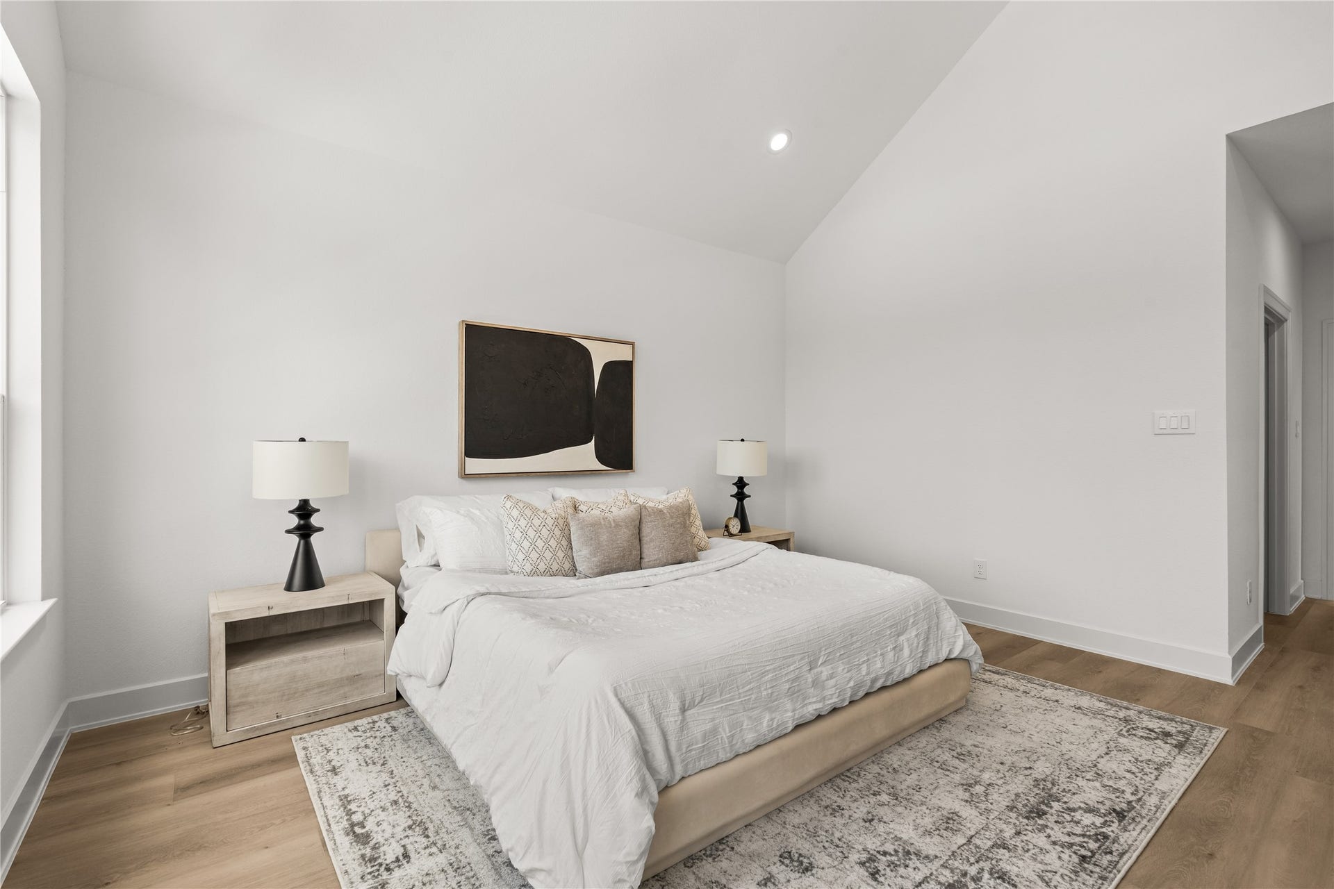 This view of the primary suite shows off its balanced layout, high vaulted ceiling, and smooth white walls.