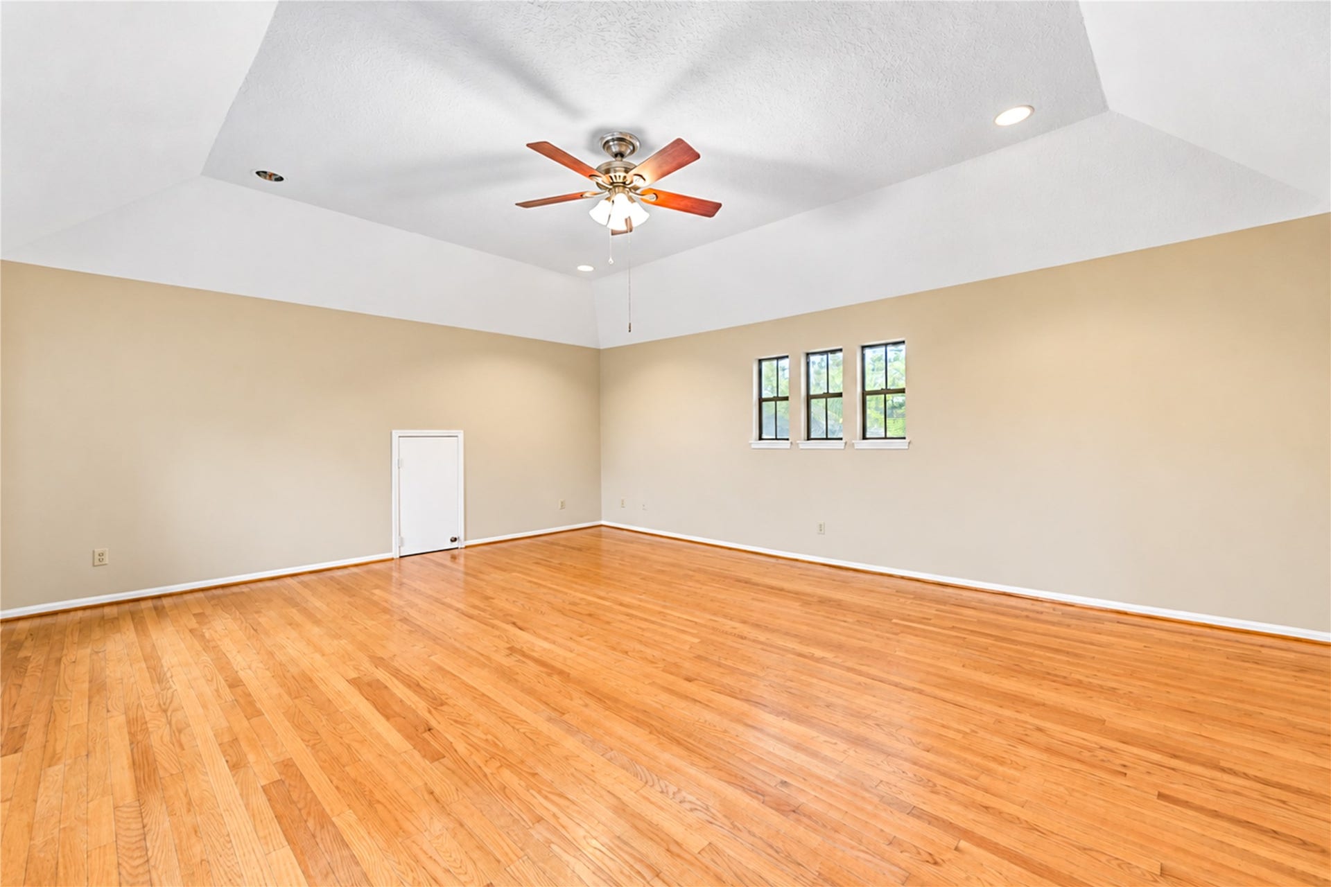 Spacious room with gleaming hardwood floors, vaulted ceiling, and a ceiling fan, perfect for versatile living arrangements.