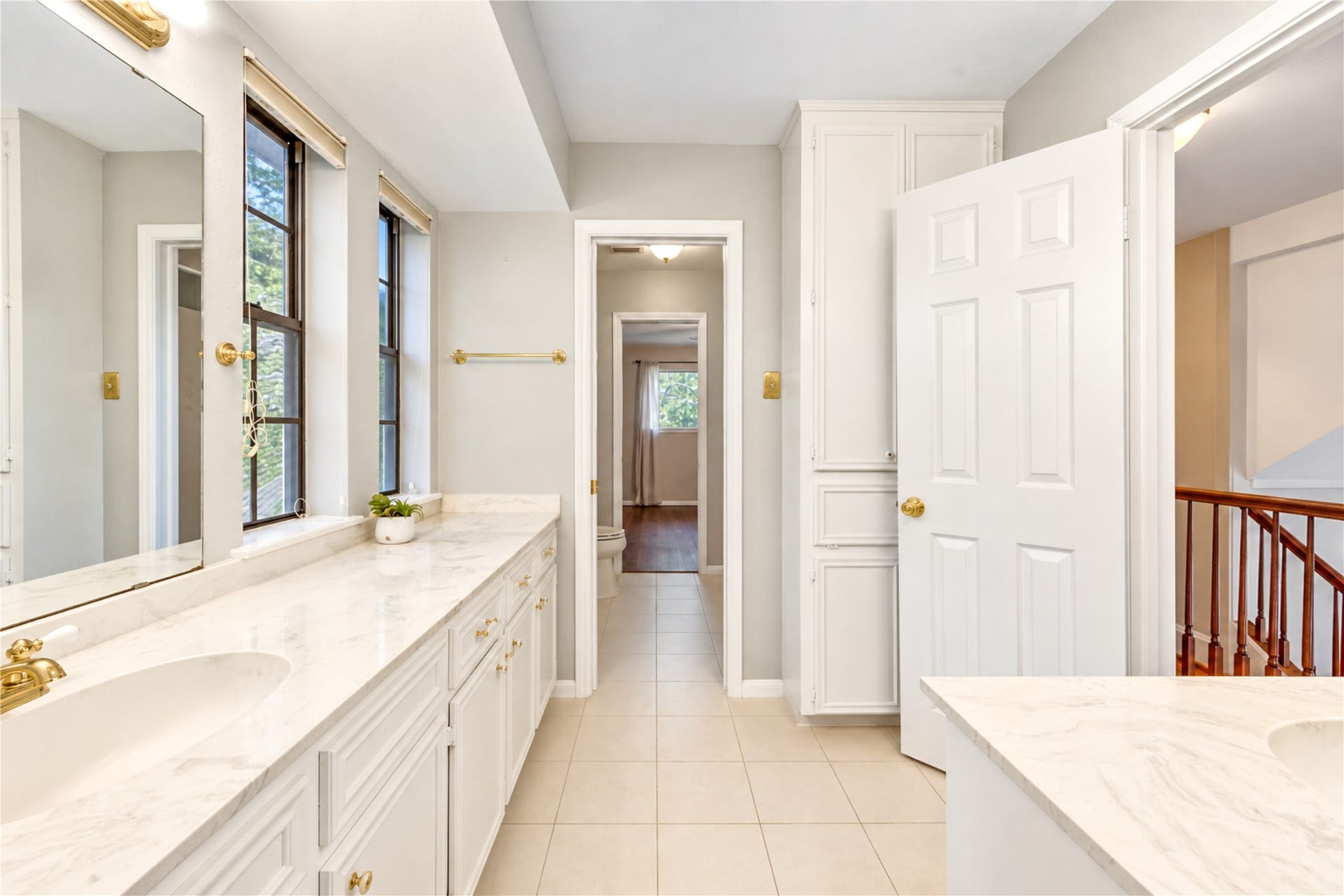 Bright and elegant bathroom featuring dual sinks with marble countertops, ample storage, and large windows for natural light.