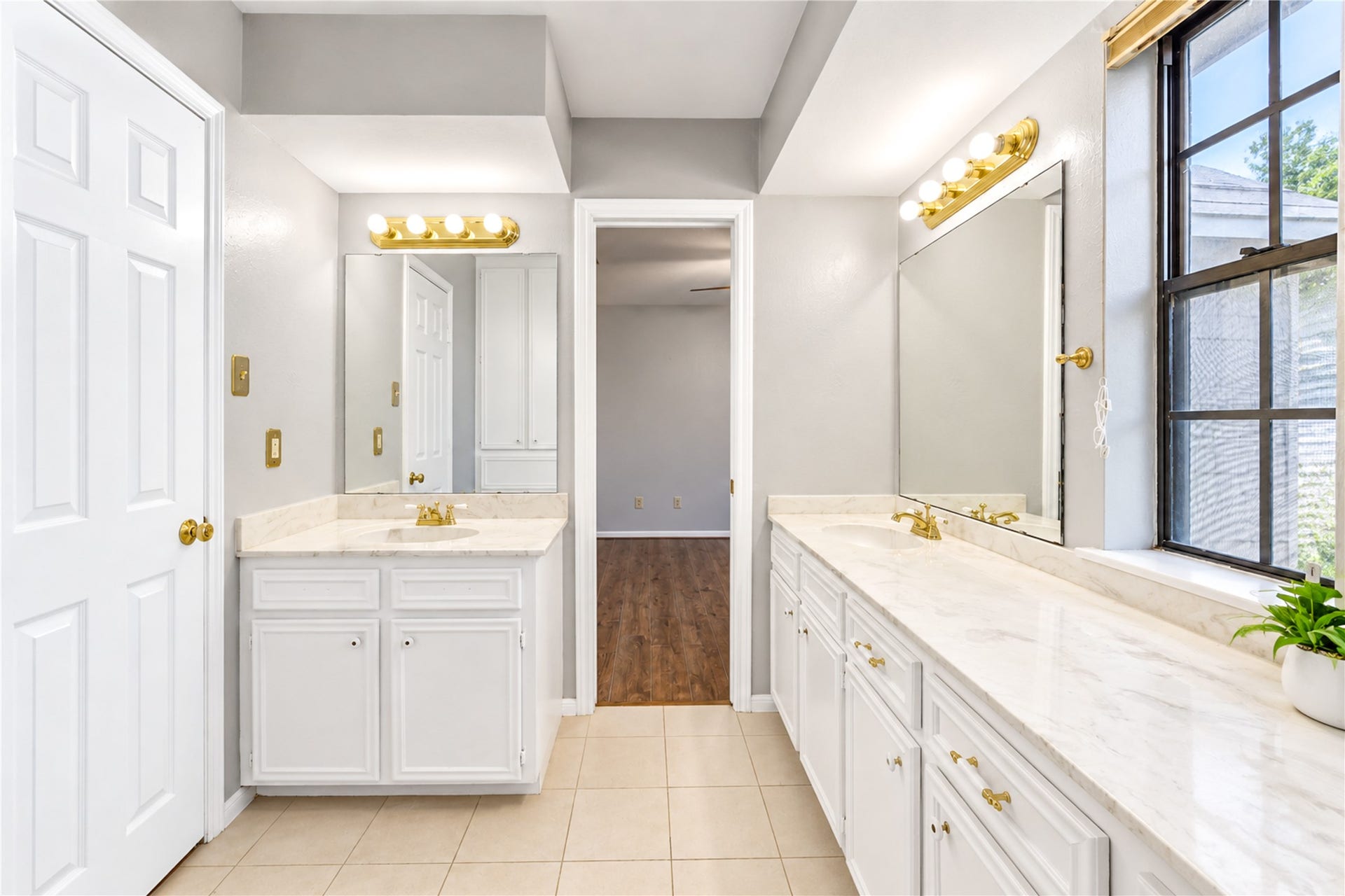 Spacious bathroom with dual sinks, elegant marble countertops, and ample natural light from a large window, offering a bright and inviting atmosphere.