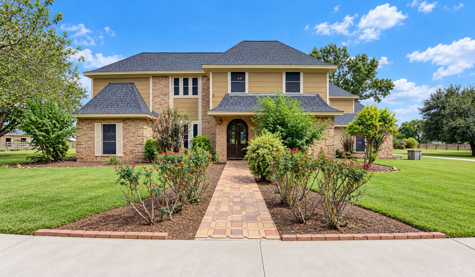 Stunning two-story home with charming brick and siding exterior, set on a beautifully landscaped lot featuring a brick walkway and lush greenery.