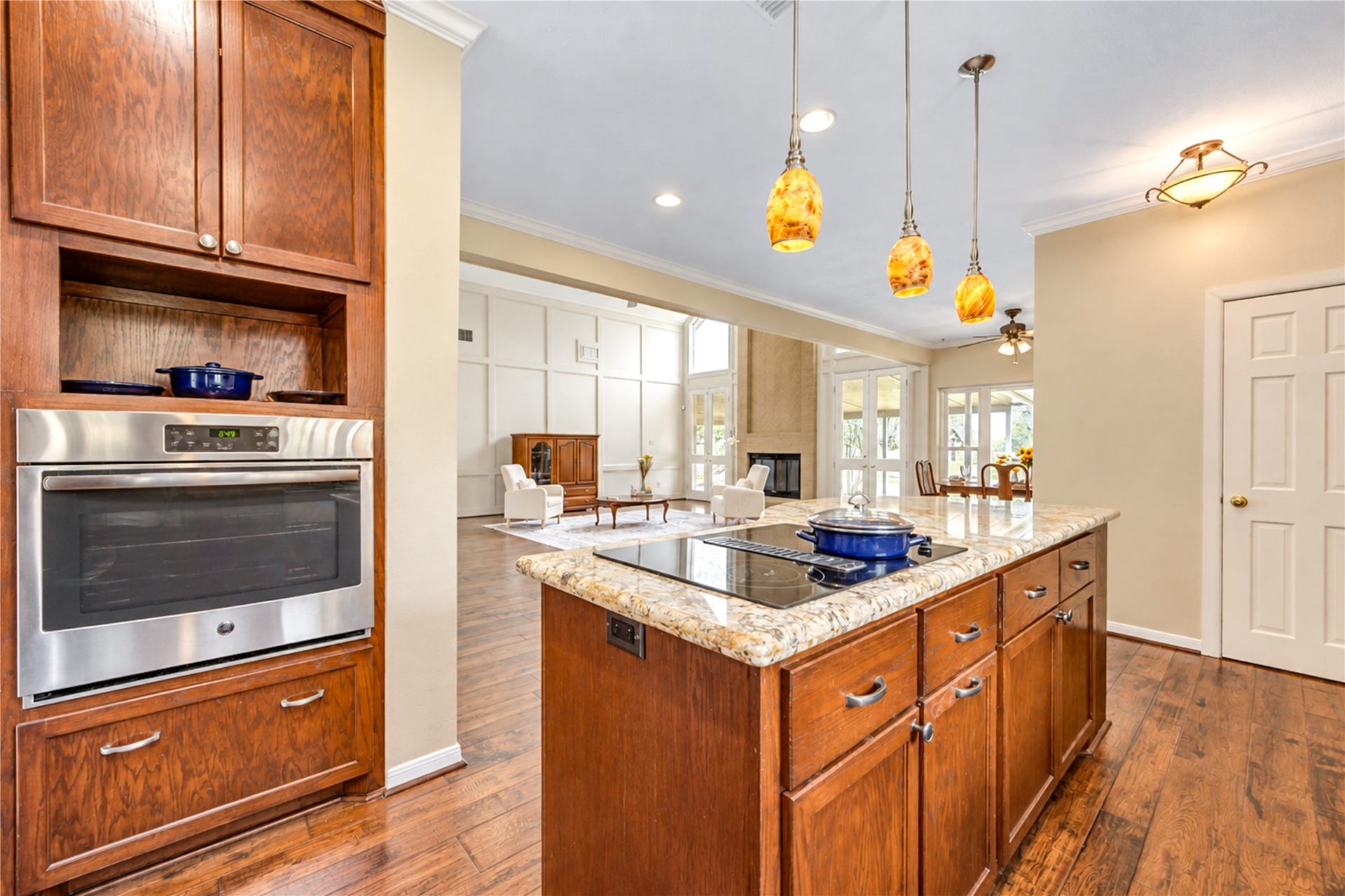 This kitchen with rich beautiful wood cabinetry, a sleek built-in oven, and a large granite island illuminated by elegant pendant lights. The open layout seamlessly connects to a bright living area with abundant natural light.