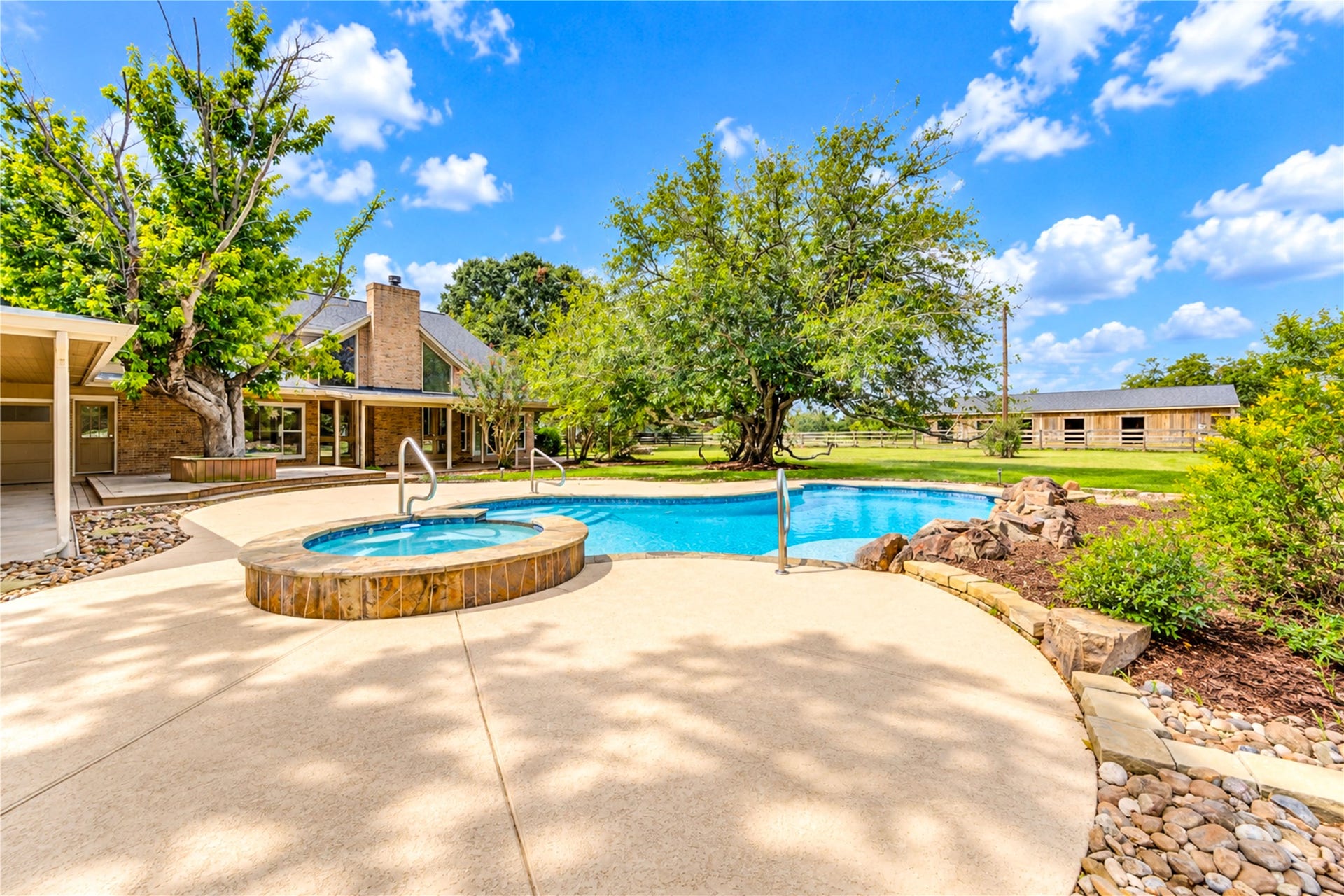 Spacious backyard oasis featuring a sparkling pool and hot tub, surrounded by lush greenery and a generous patio area perfect for relaxation and entertaining.