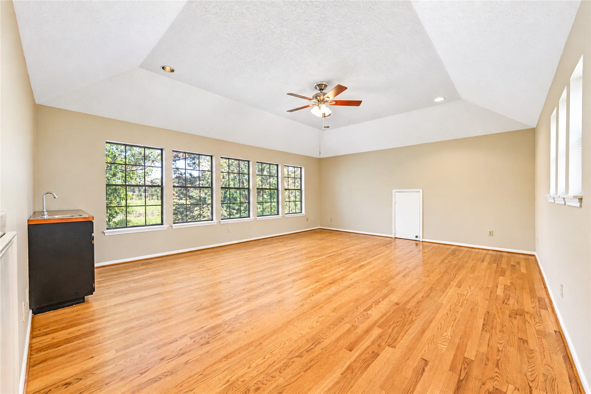 Spacious room with vaulted ceilings, abundant natural light from large windows, and elegant hardwood flooring, perfect for versatile living or entertaining.