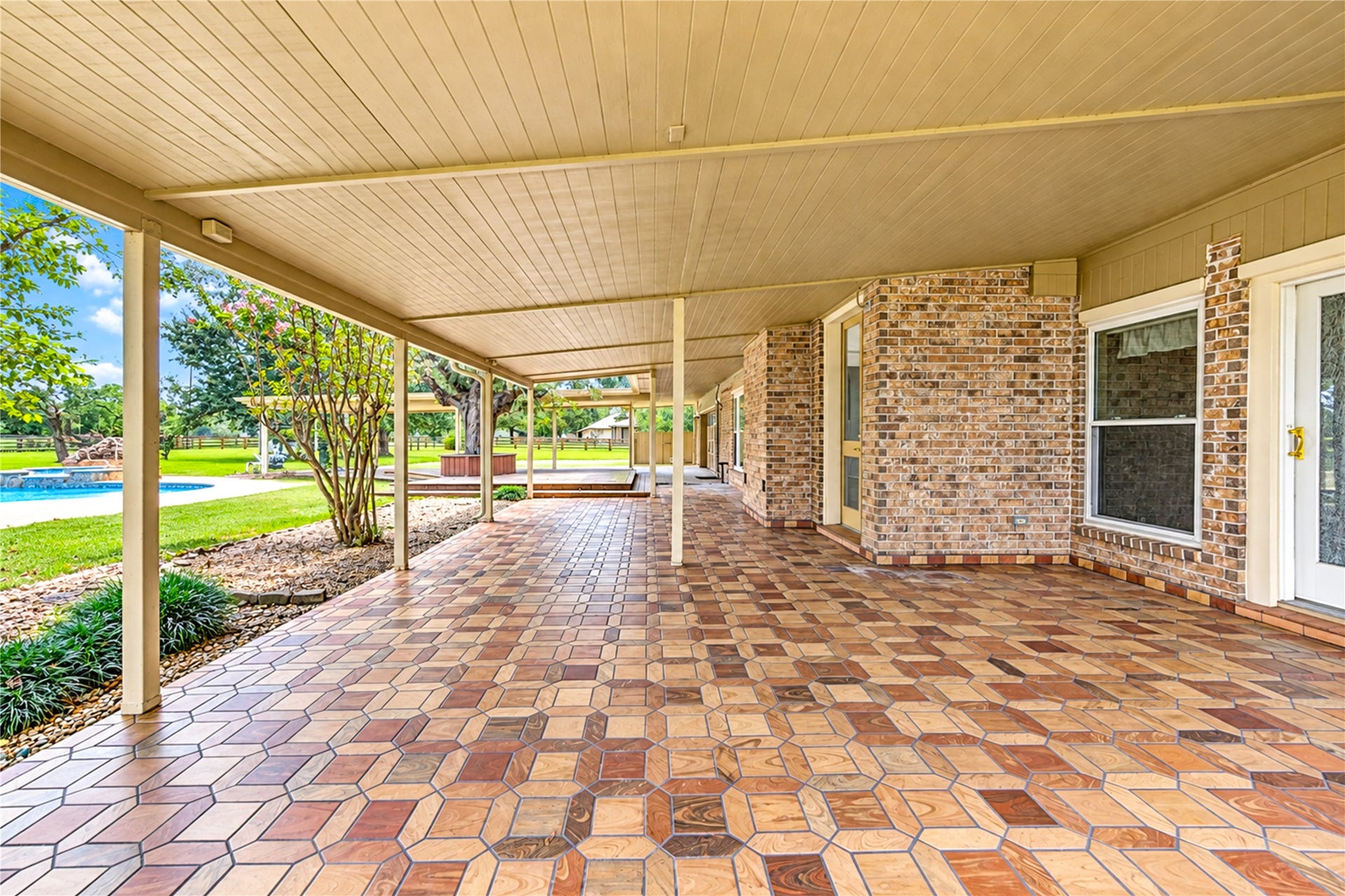 Spacious covered patio with elegant tile flooring, perfect for outdoor entertaining, complemented by a lush garden view and inviting pool.