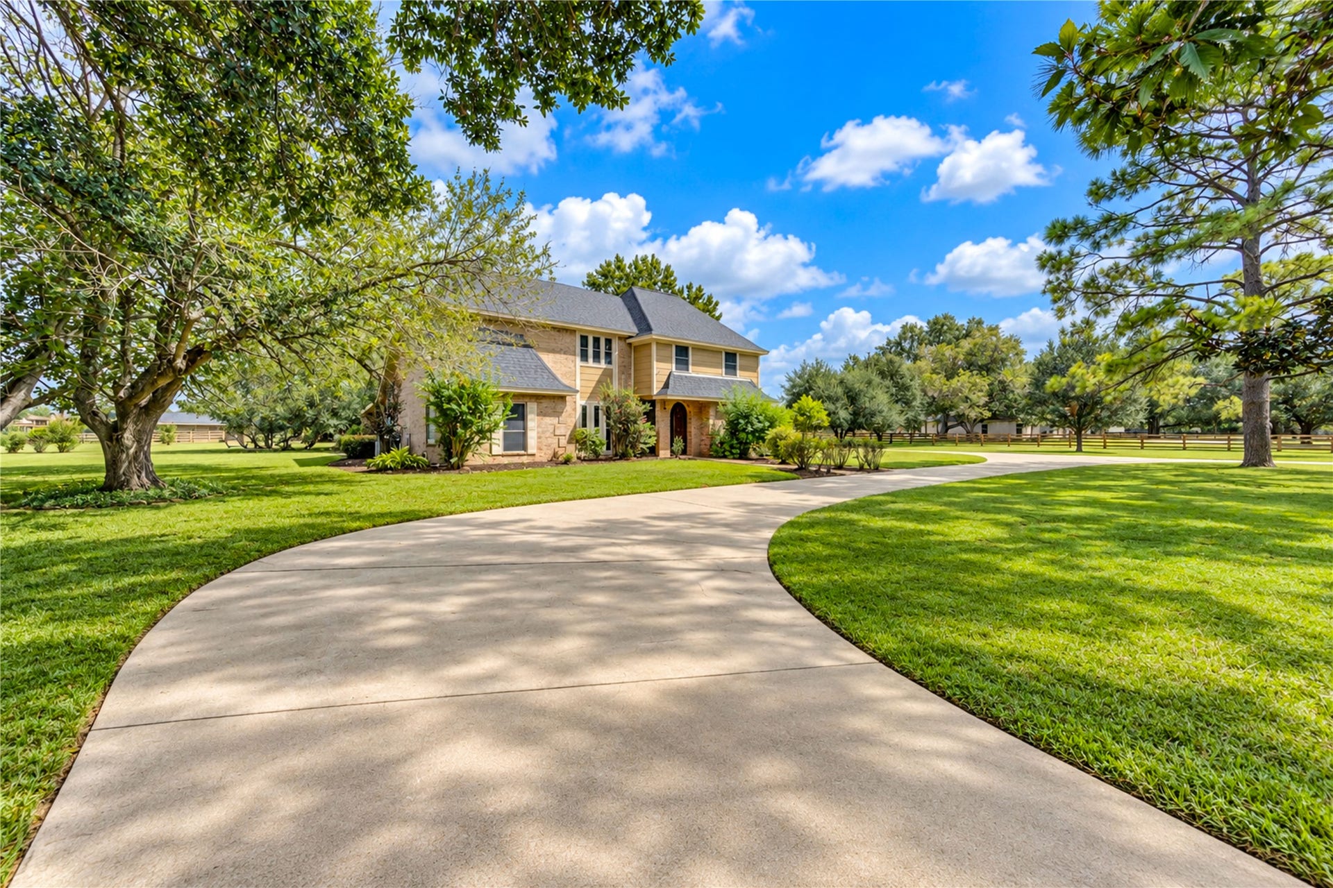Stunning two-story home nestled on a sprawling, manicured lawn with a charming curved driveway and mature trees providing ample shade and privacy.