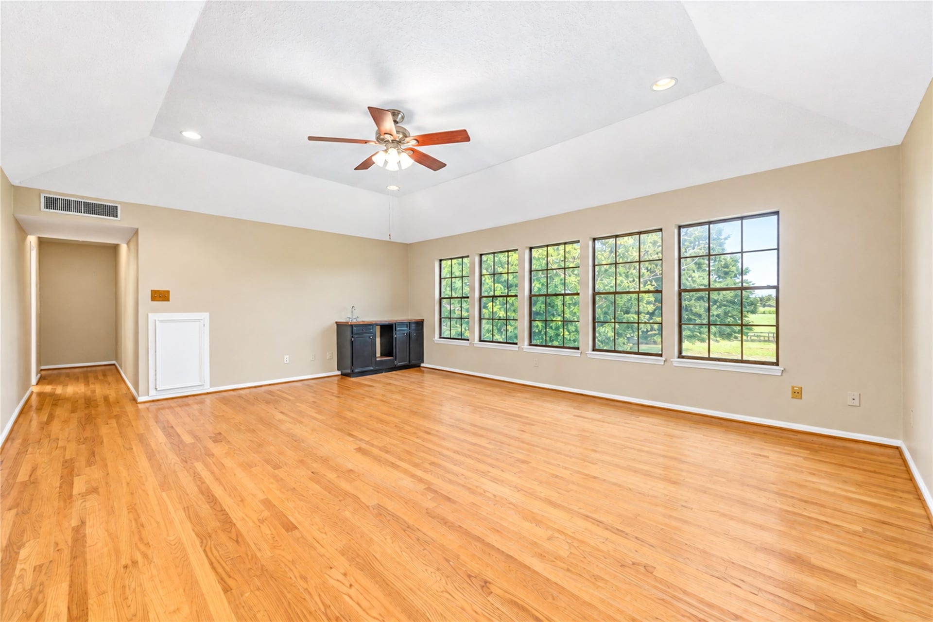 Spacious room with gleaming hardwood floors and a vaulted ceiling, featuring large windows that offer abundant natural light and scenic views.