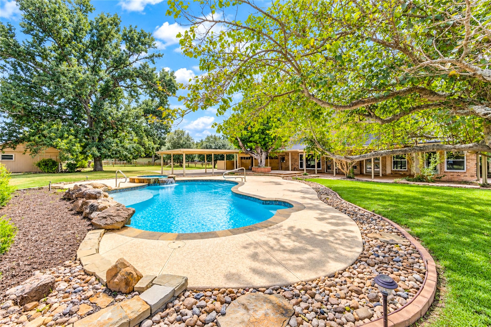 Enjoy the serene backyard oasis featuring a sparkling pool surrounded by lush greenery and mature trees, perfect for relaxation and outdoor entertaining.