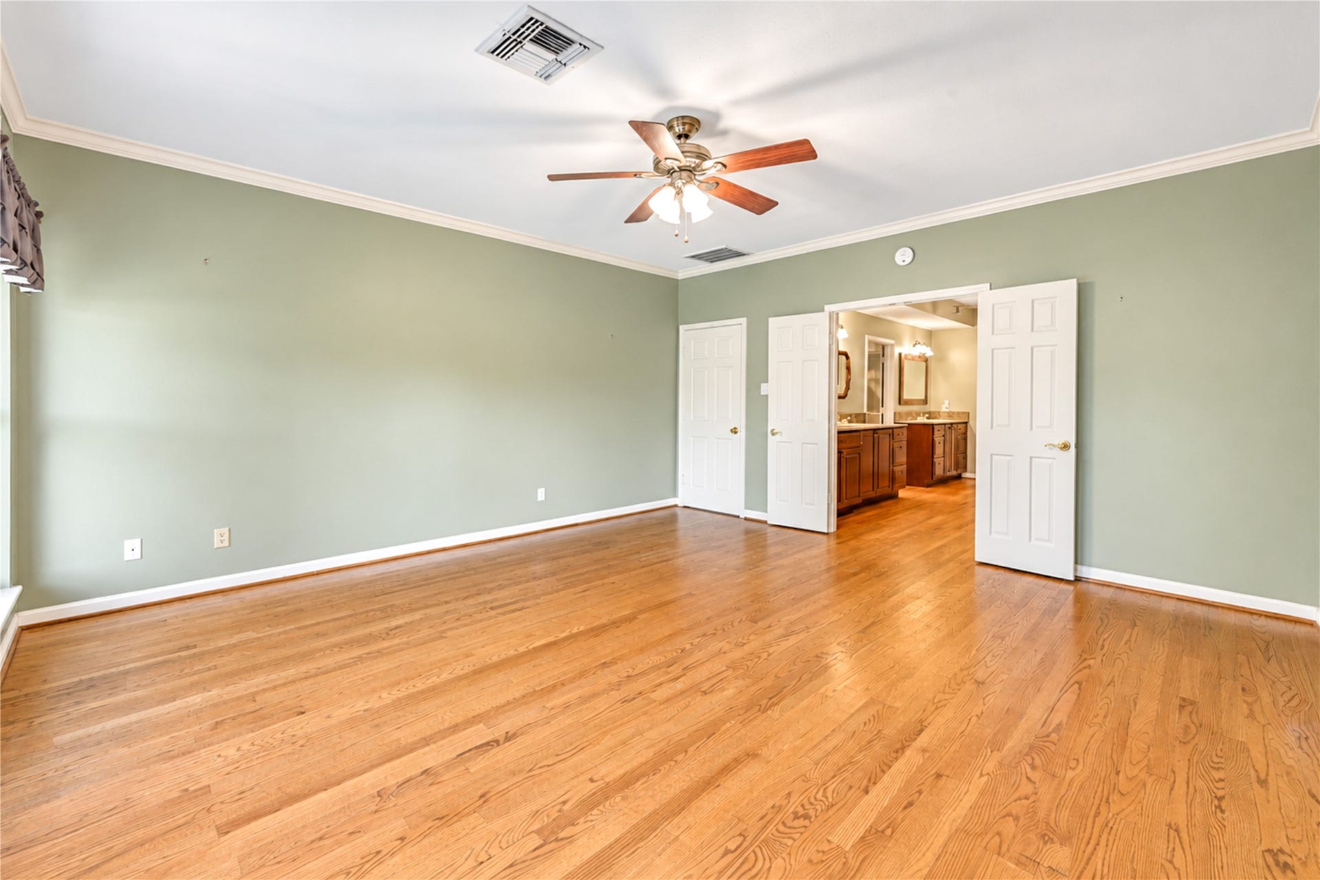 The primary bedroom features elegant hardwood floors and leads to an en-suite bathroom with double doors, the primary closet and backyard patio through sliding doors.