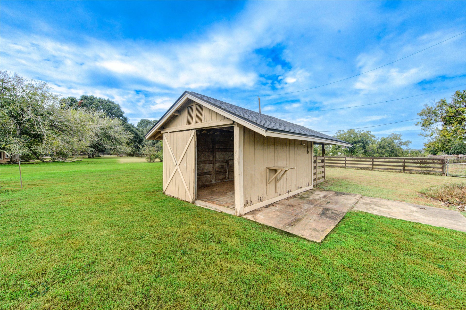 Charming wooden outbuilding set in a spacious, lush green yard, perfect for storage or creative use, surrounded by a serene rural landscape.
