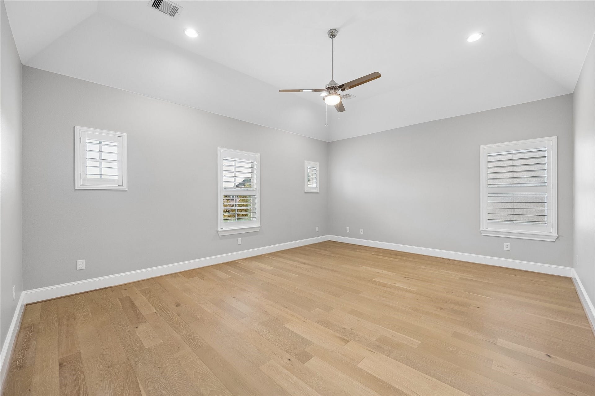6029 Matthew Oaks Place, Houston, TX 77007 Primary bedroom. Spacious room with high ceilings, elegant light wood flooring, and ample natural light from multiple Plantation shuttered window treatments, complemented by a modern ceiling fan.