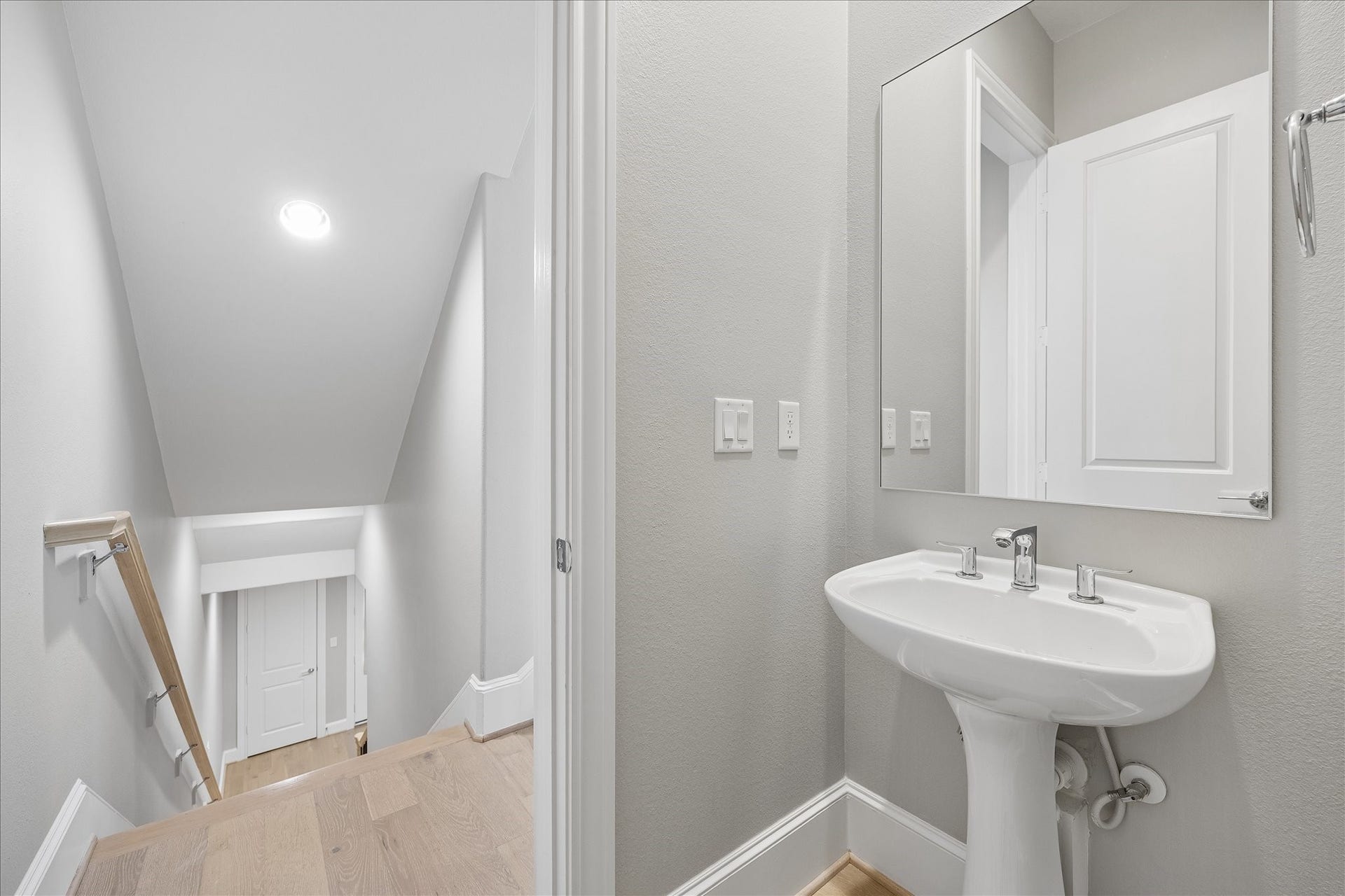 6029 Matthew Oaks Place, Houston, TX 77007 Stylish half-bath featuring a modern pedestal sink and mirror, conveniently located away from the living area and near a bright staircase with sleek wooden handrails.