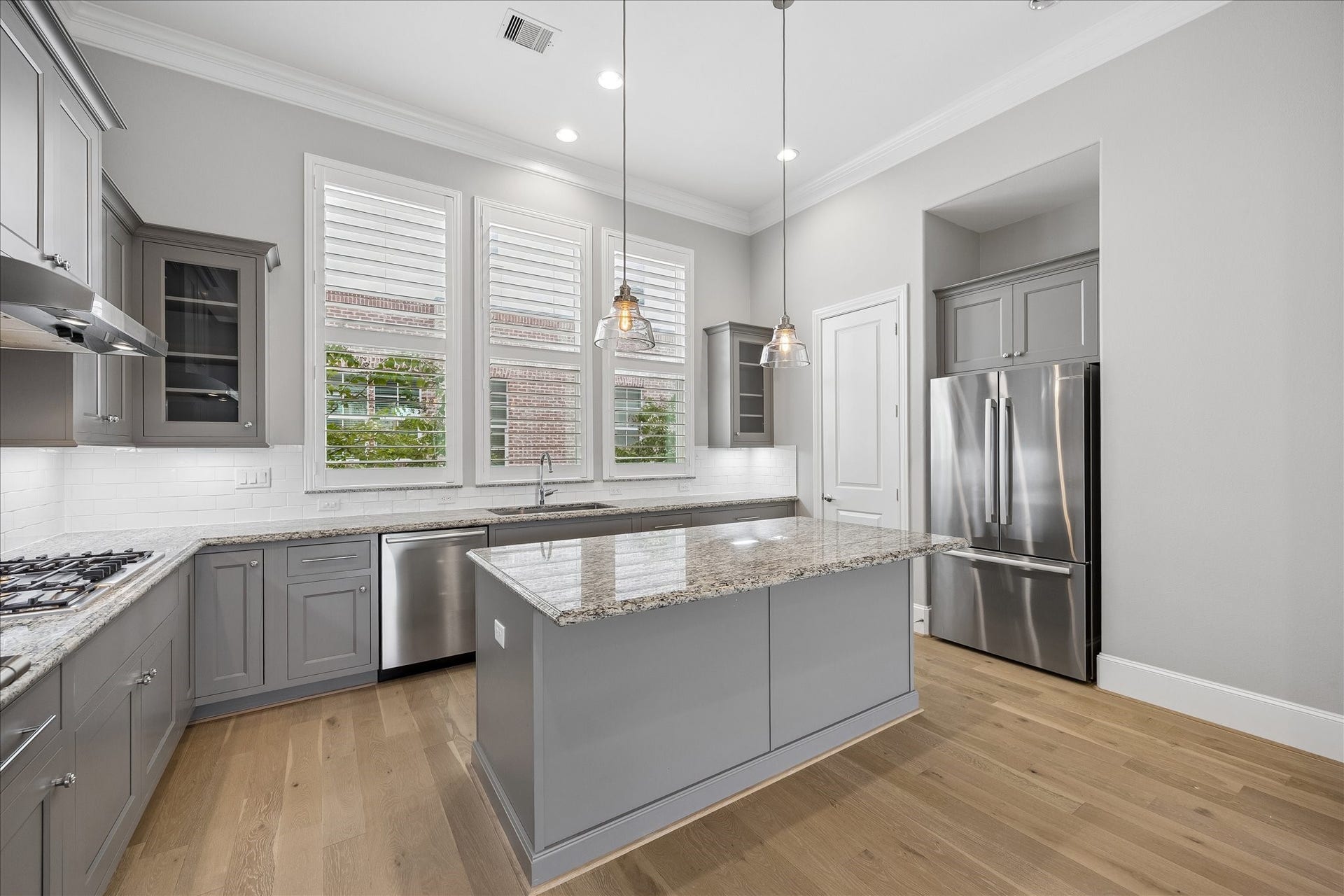 6029 Matthew Oaks Place, Houston, TX 77007 Modern kitchen with sleek gray cabinetry, a spacious granite-topped island, and stainless steel appliances. Open to living area and walk-in pantry. Refrigerator included.