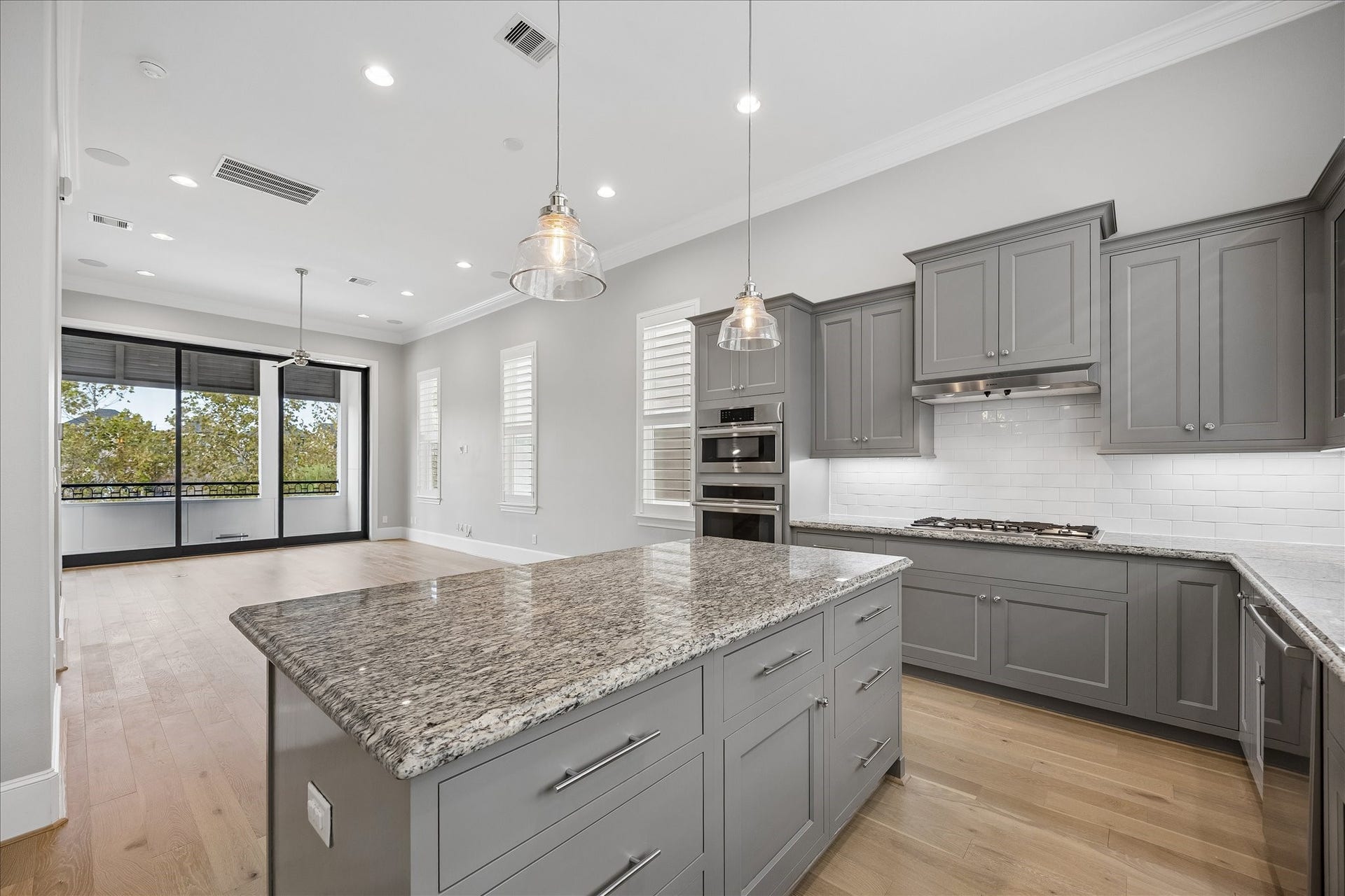 6029 Matthew Oaks Place, Houston, TX 77007 Spacious modern kitchen with sleek gray cabinetry, granite countertops, and stainless steel appliances, opening to a bright living area overlooking the Lake with fountain view and large windows and hardwood floors.