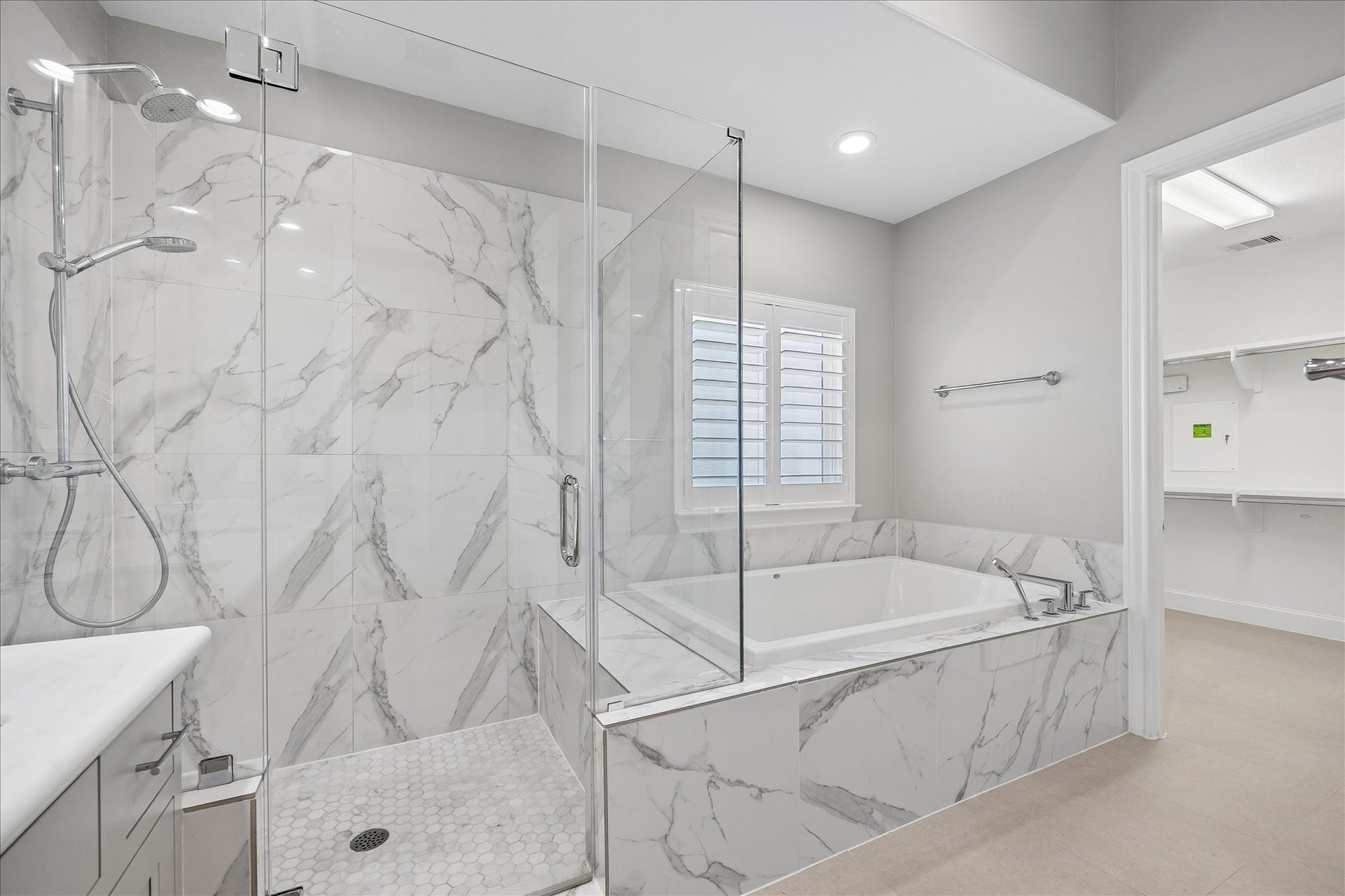 6029 Matthew Oaks Place, Houston, TX 77007 Luxurious bathroom with elegant marble tiles, featuring a spacious glass-enclosed shower and a relaxing soaking tub beneath a bright window.