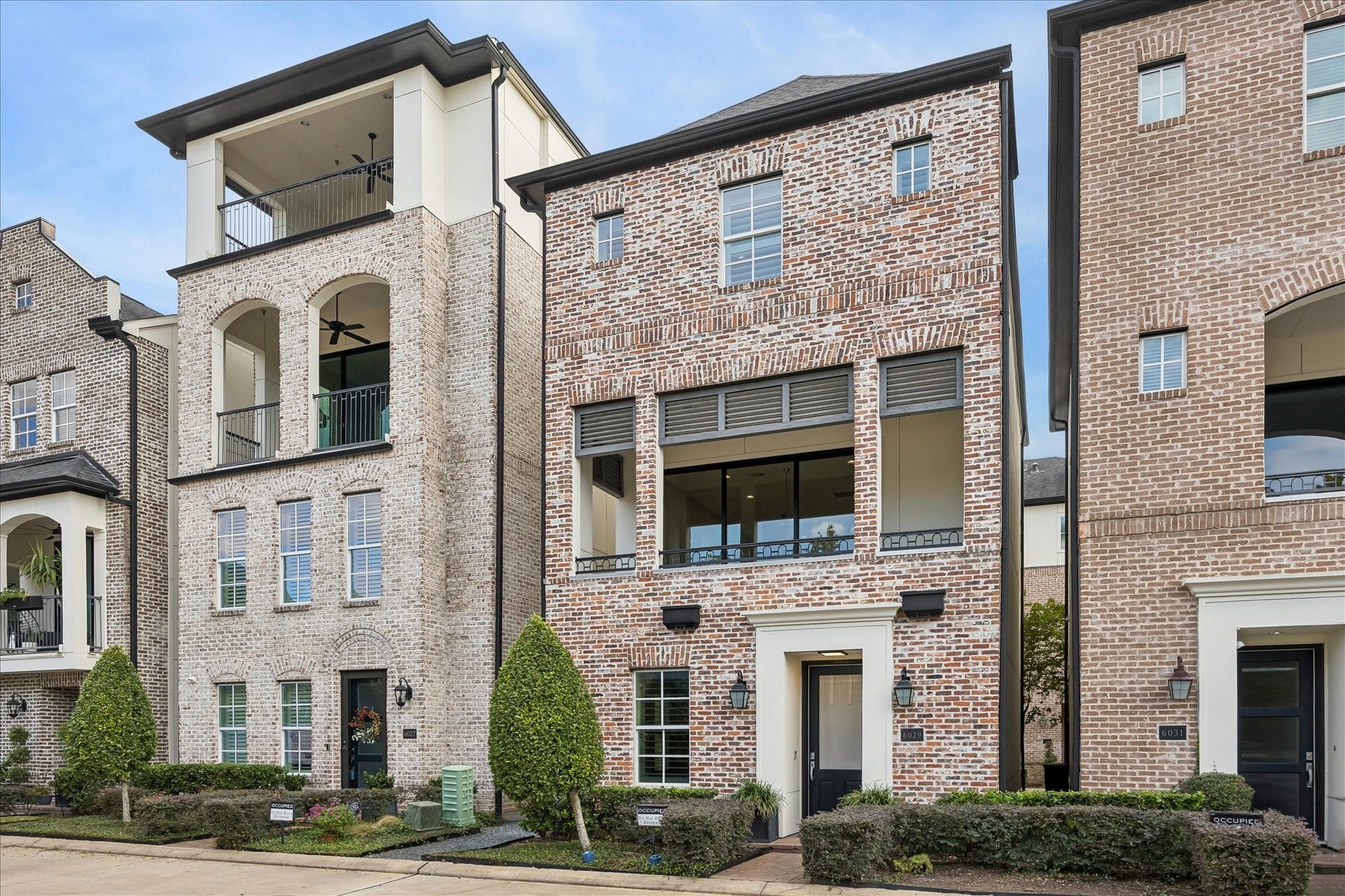 6029 Matthew Oaks Place, Houston, TX 77007 Elegant 3-story single family home with a classic brick facade, large windows, and a charming covered balcony overlooking water and fountain.