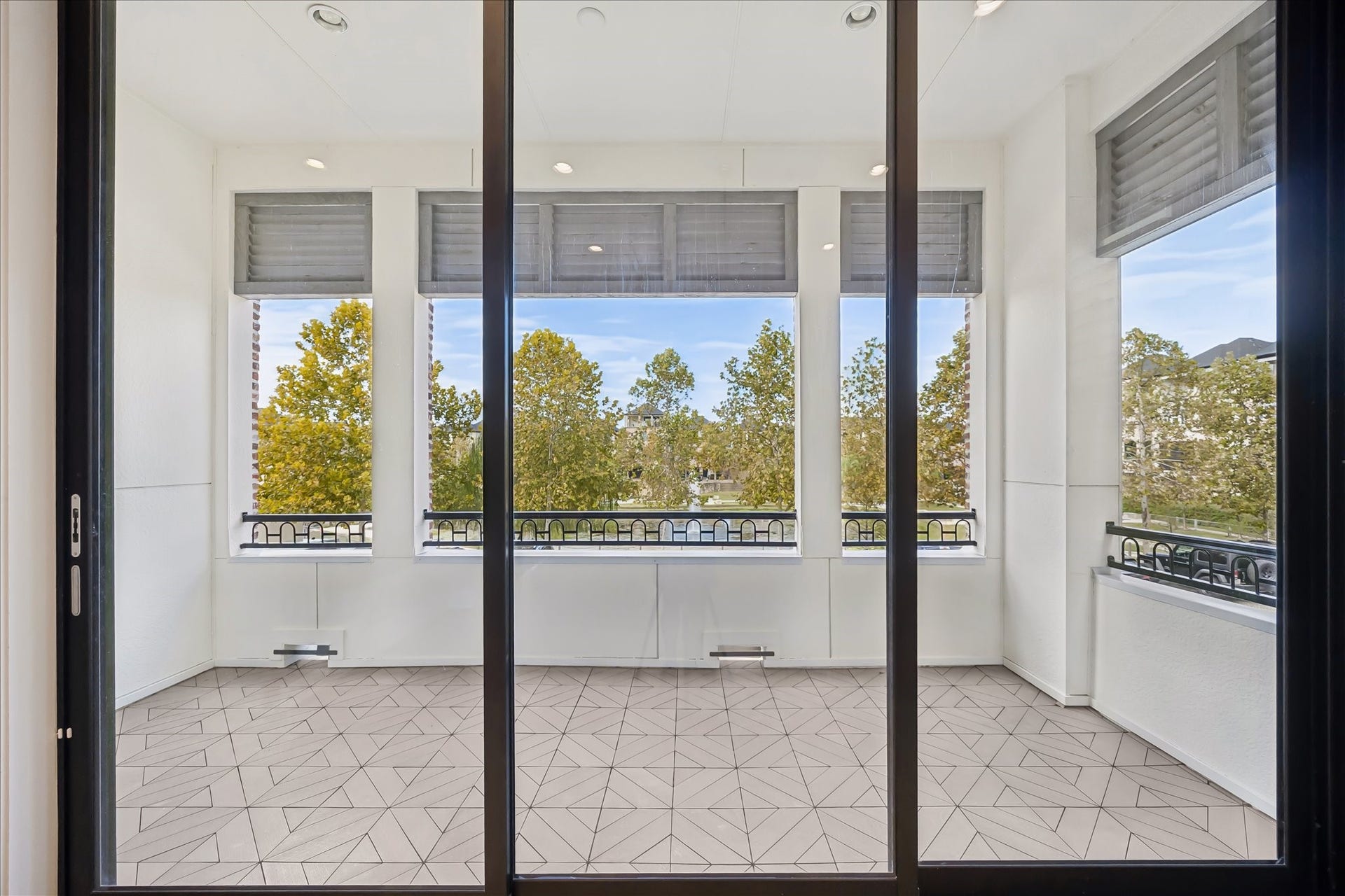 6029 Matthew Oaks Place, Houston, TX 77007 Spacious balcony with large windows offering serene views of lush trees, Lake, and fountain with stylish tiled floor, perfect for relaxation or entertaining. The 3 panel windows/sliding glass doors open. See previous pictures.