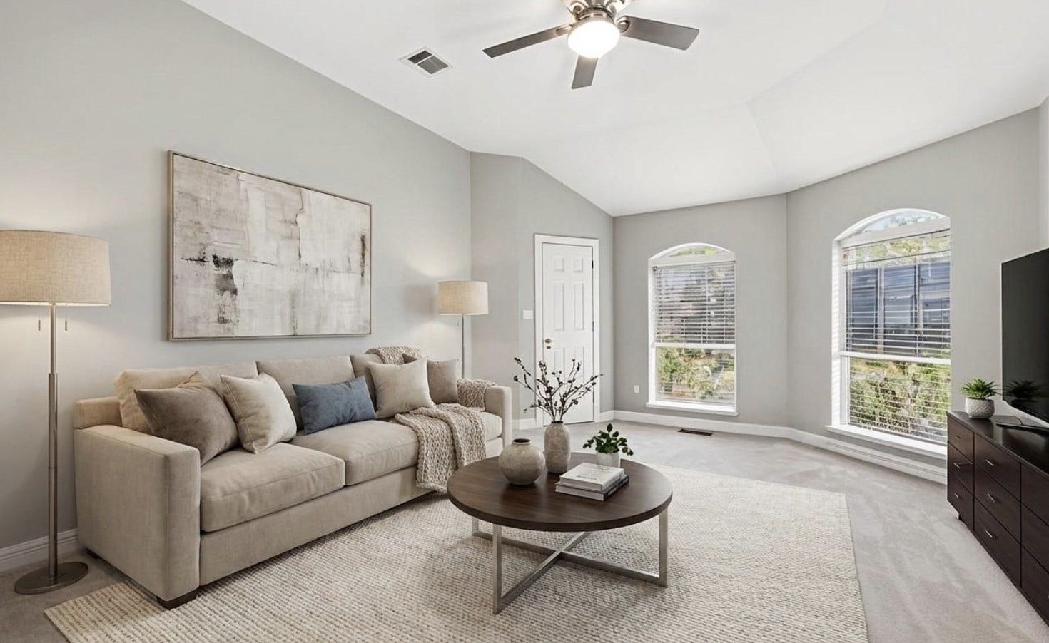 A light-filled family room with an angled ceiling and arched-top windows offers a comfortable, open gathering space finished in neutral tones. (Virtually staged).