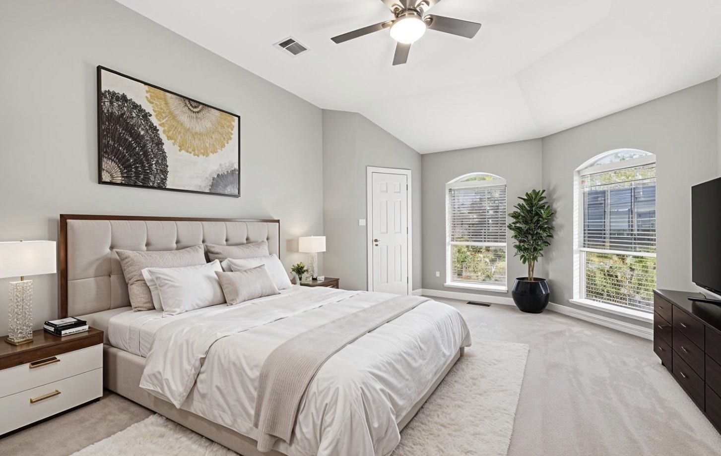 A primary bedroom with a vaulted ceiling and a centered ceiling fan offers soft carpet underfoot and two arched-top windows that bring in natural light. (Virtually Staged.