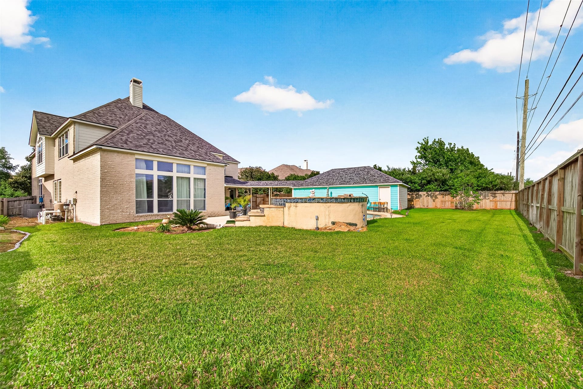 The rear elevation opens to a broad lawn framed by a covered patio and a bank of tall, white-framed windows that draw natural light across the back of the home. A detached outbuilding finished in blue siding and a wood privacy fence complete the private backyard setting.