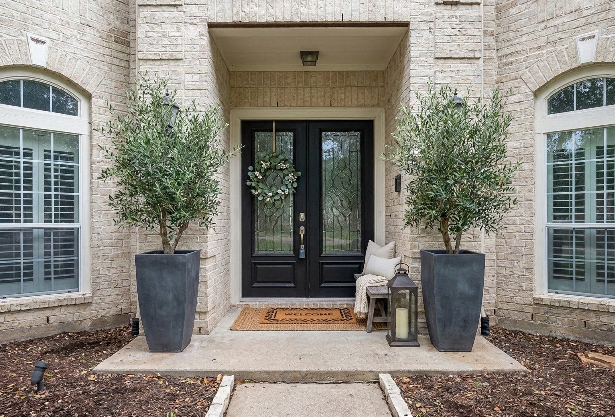 A recessed covered entry framed in cream brick introduces the home, where glass-paneled double doors with decorative wrought-iron detailing are flanked by arched windows. Concrete steps and a stone-edged walkway lead through a landscaped bed to the stoop, completing a polished first impression.(Virtually Staged)