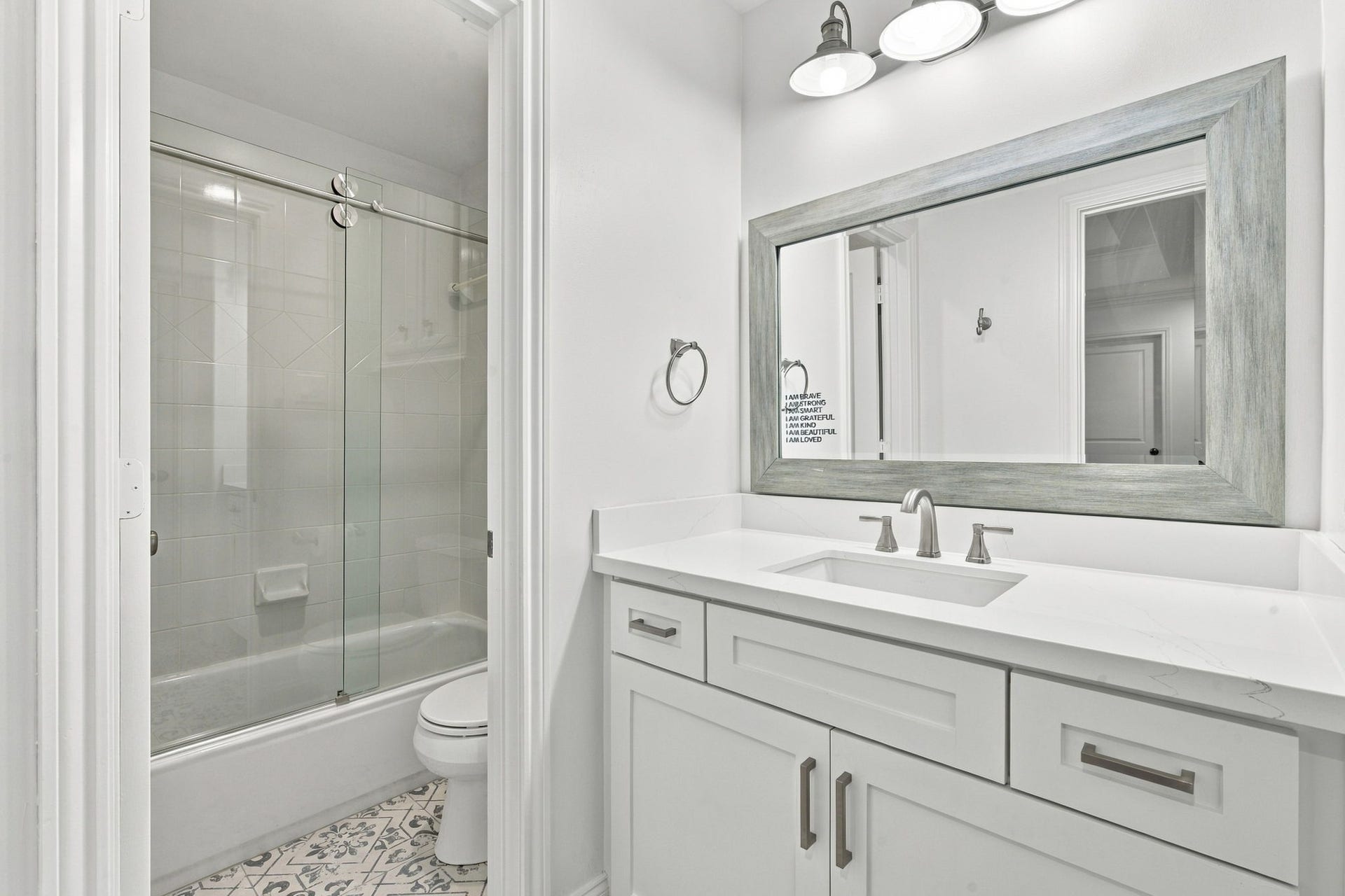 Beautiful full bath featuring a vanity w/stone countertop, undermount sink, white cabinetry & updated fixtures. Separate bathing area includes a tub/shower combination w/sliding glass doors & decorative tile flooring.