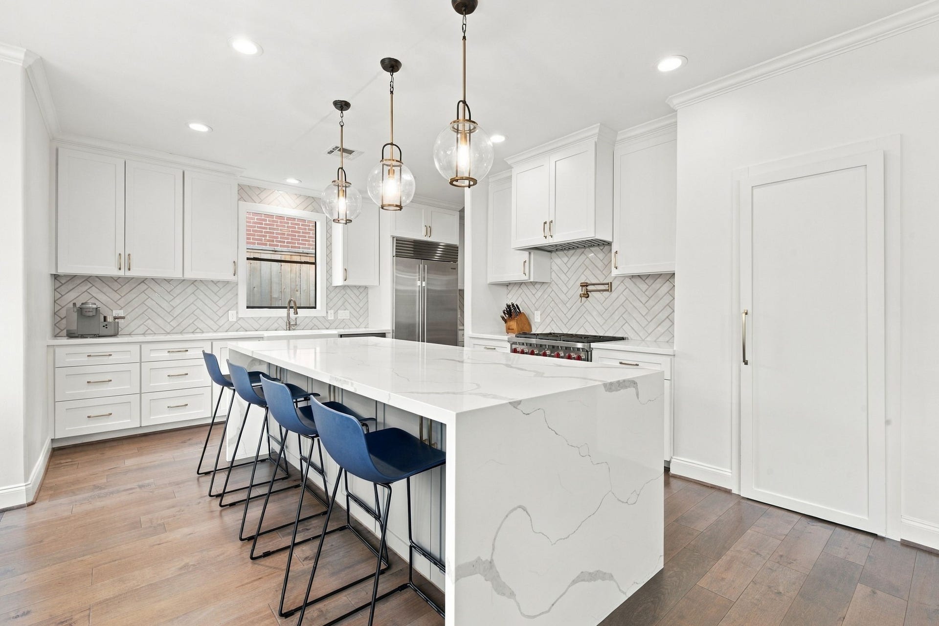 The expansive island offers breakfast bar seating for four, making it a wonderful gathering spot for casual meals & entertaining. Three beautiful glass pendant lights illuminate the space, while the professional-style gas range, custom cabinetry & generous counter space enhance this thoughtfully designed kitchen.
