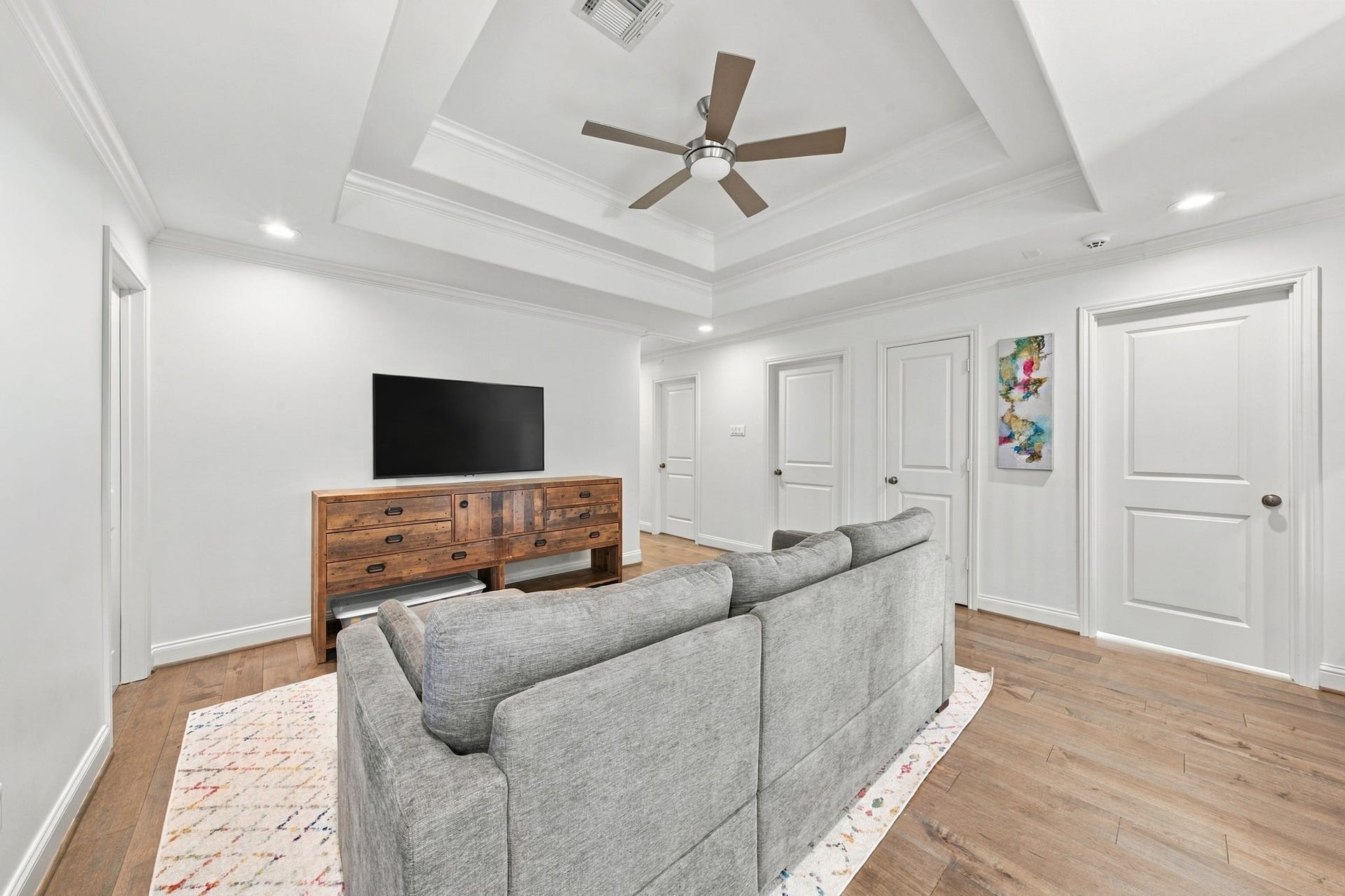 Upstairs game room showcasing the beautiful tray ceiling, crown molding, hardwood floors & easy access to the surrounding bedrooms. A versatile gathering space ideal for relaxation, recreation or movie nights!