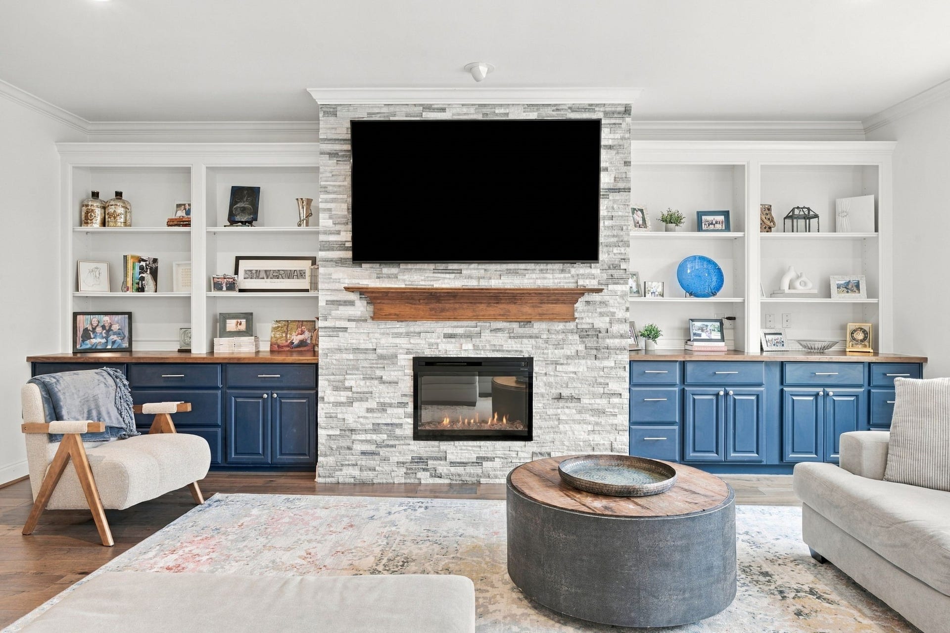 The impressive fireplace serves as the focal point of the living room, featuring beautiful, stacked stone, a rich wood mantel & space for a mounted television. Flanking custom built-ins offer open display shelving, contrasting blue lower cabinetry & wood countertops, combining style & functionality.