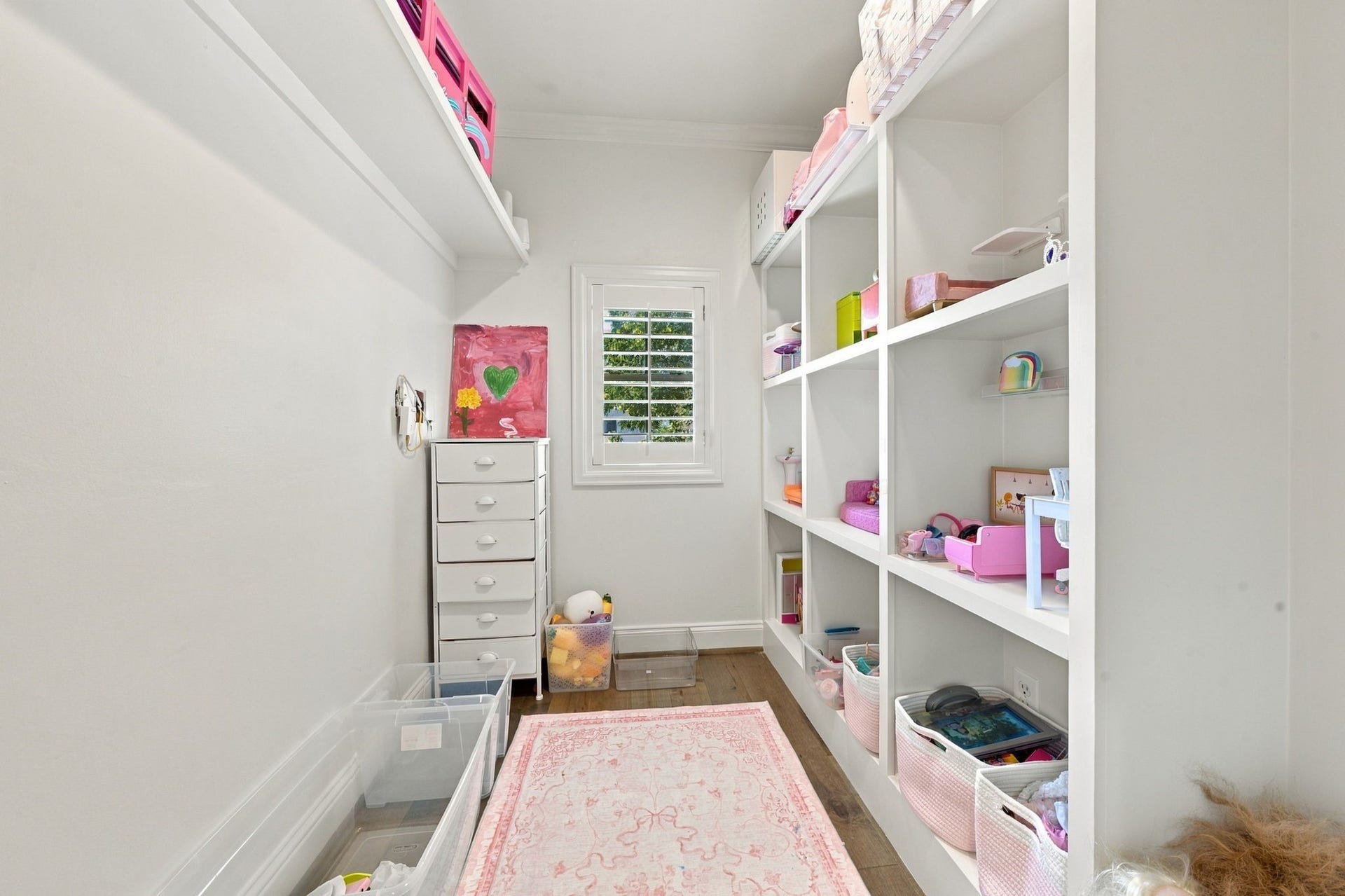 Inside the dollhouse, discover a delightful playroom featuring built-in shelving, hardwood floors & a window w/plantation shutters. Wonderful space for creative play, toys & organized storage!