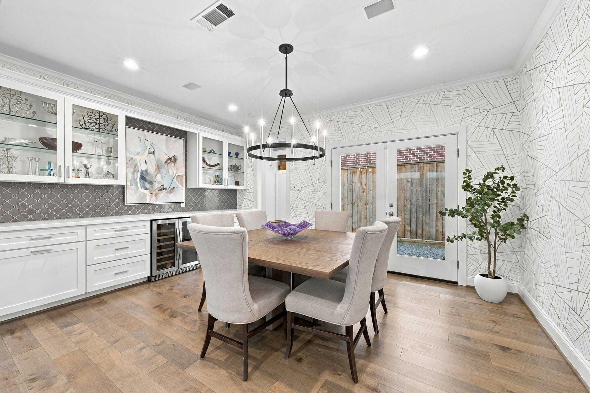 Another perspective highlights the thoughtfully designed built-in serving area, with wine refrigerator, offering extensive countertop space for hosting & displaying your favorite pieces. French doors provide convenient outdoor access, while recessed lighting & crown molding complete this beautifully appointed space.